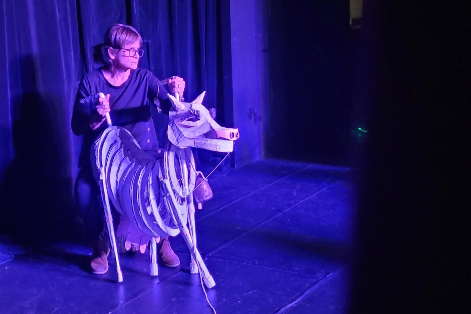 Jen operating Milky White puppet for Into the Woods production, washed in deep blue light. Cow reared back, head held high.