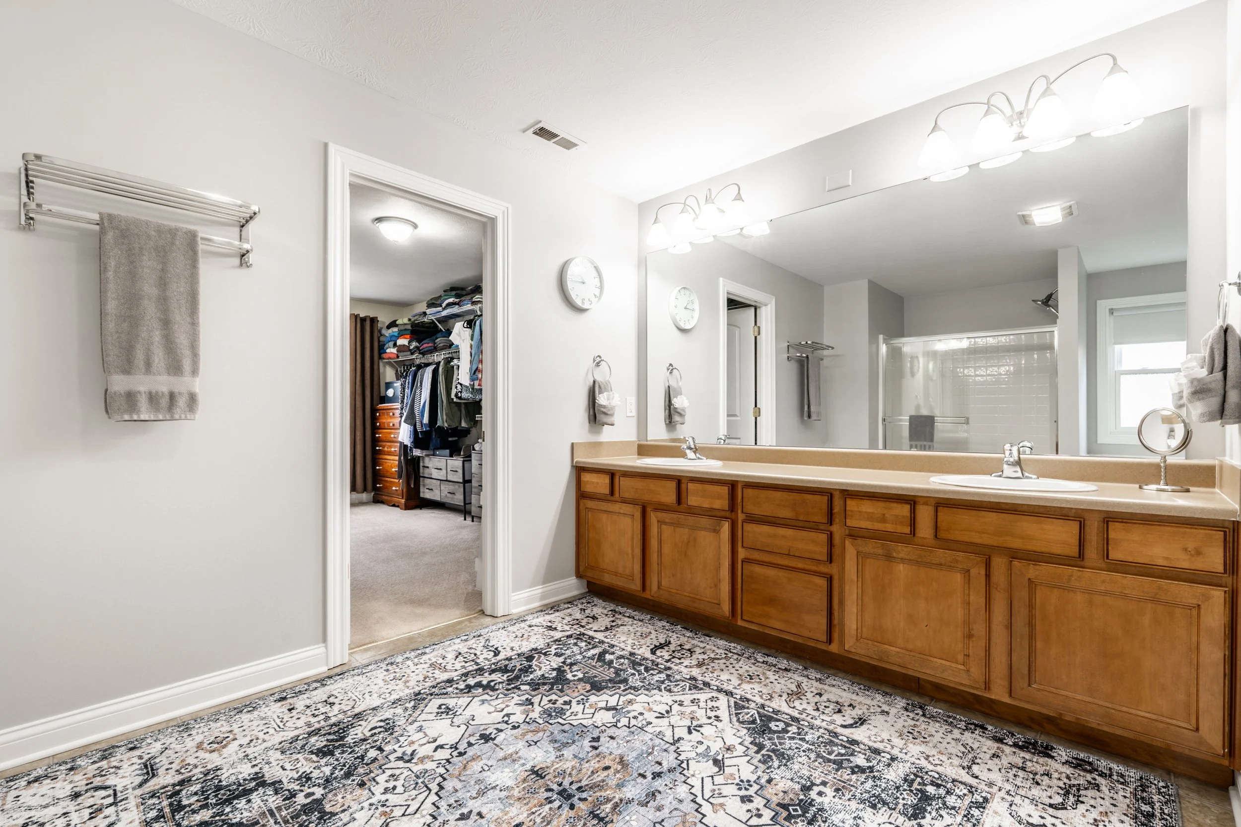 Modern bathroom with dual sinks, large mirror, and doorway to walk-in closet.