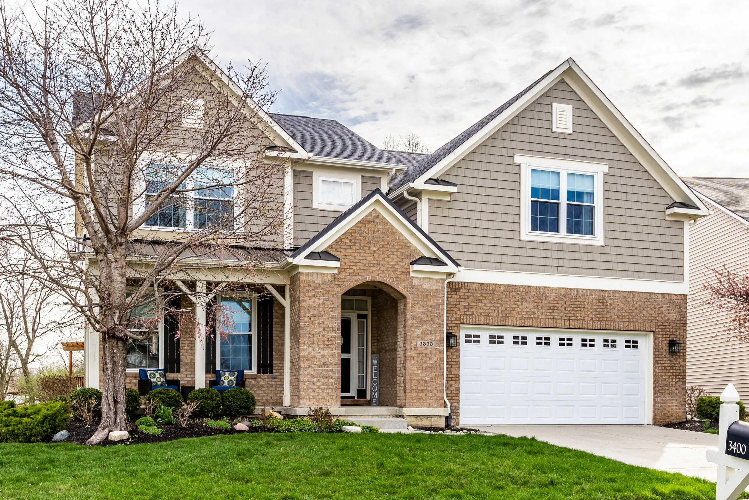 Suburban two-story house with brick and siding exterior, two-car garage, and landscaped front yard.
