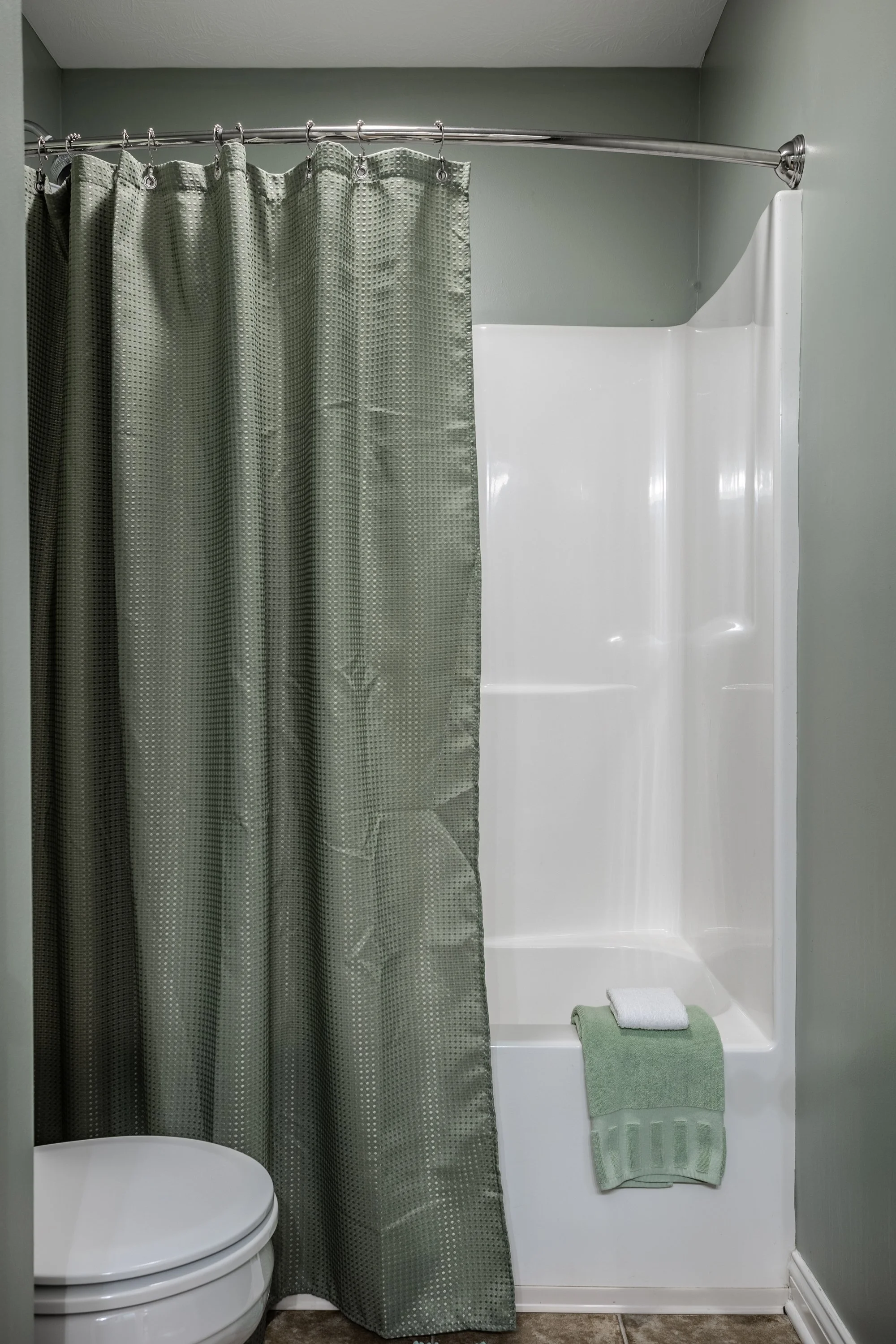 Bathroom with green shower curtain and white tub, green towel on tub edge, and white toilet.