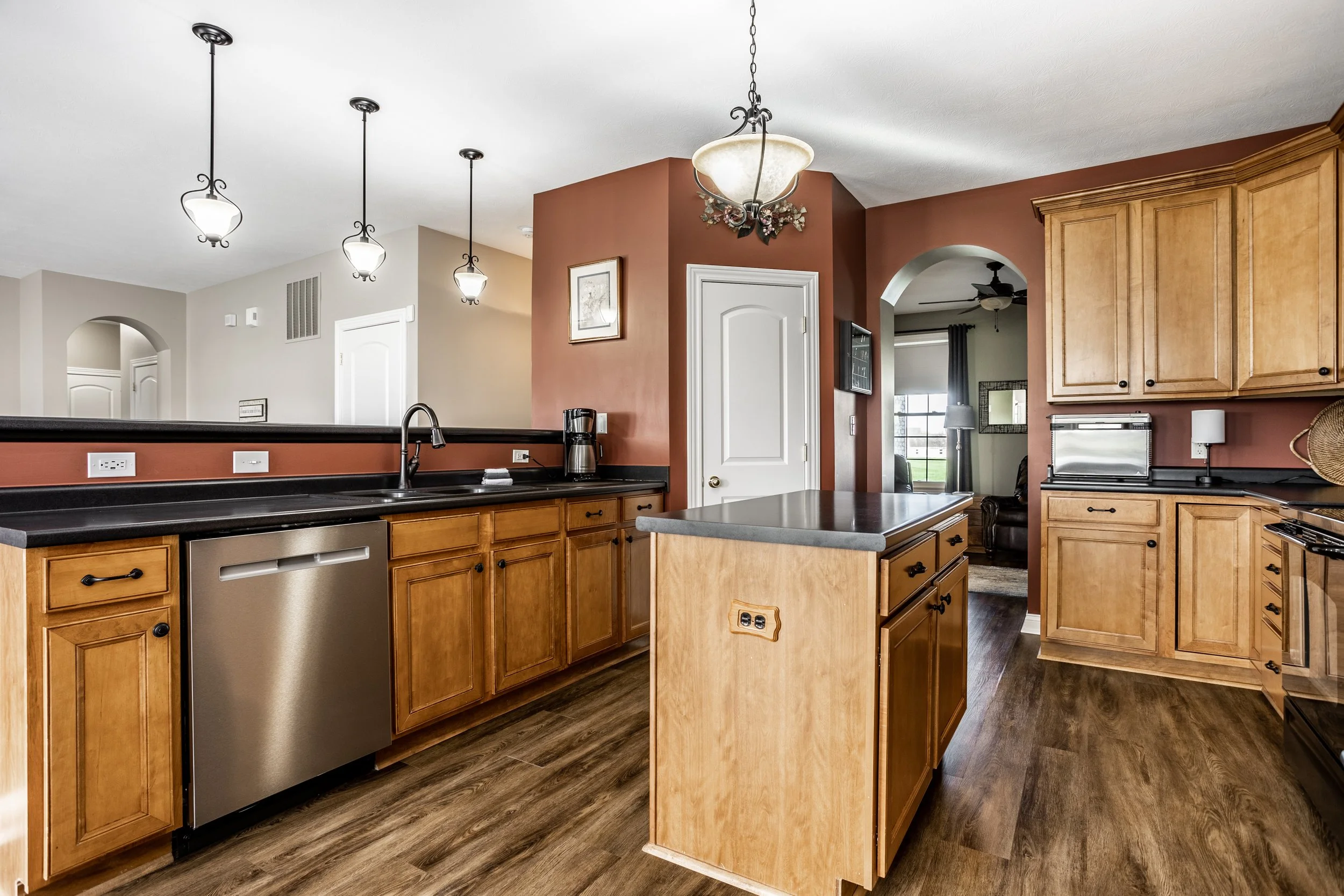 Modern kitchen with wooden cabinets, stainless steel dishwasher, island, pendant lighting, and hardwood floor.