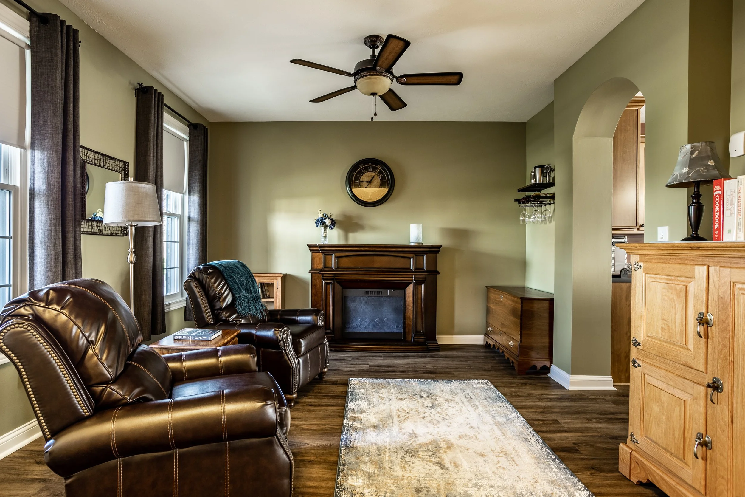 Cozy living room with leather recliners and fireplace, neutral decor, ceiling fan, and wooden furniture.