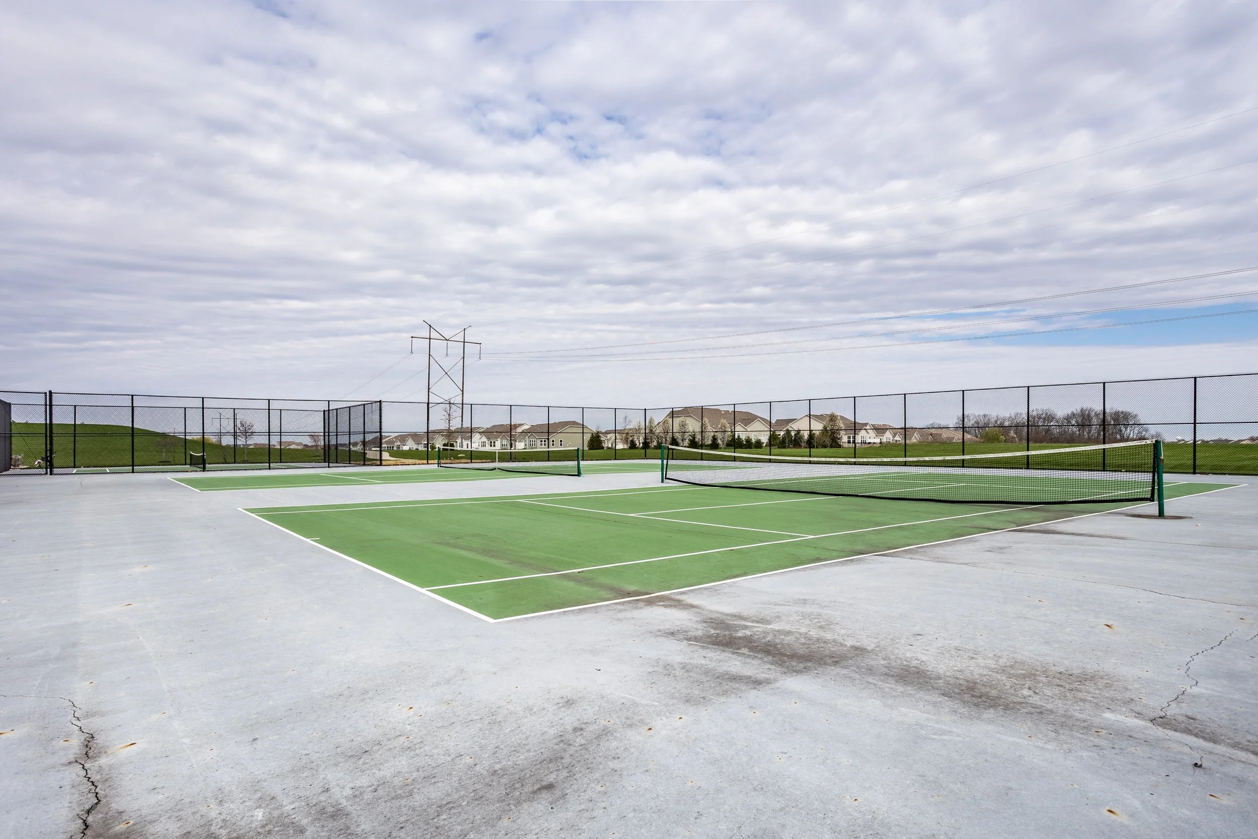 Outdoor tennis courts with fences and a cloudy sky.