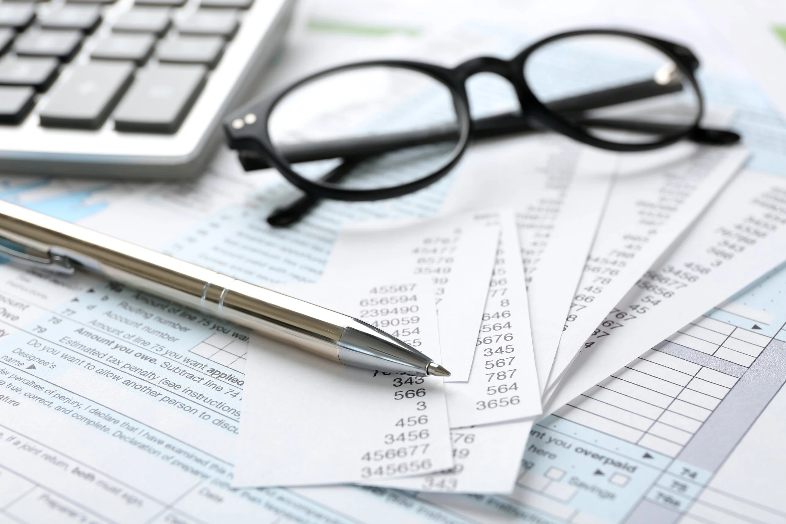 Silver pen and black reading glasses resting on IRS tax forms and receipts, illustrating recent IRS news and tax law updates