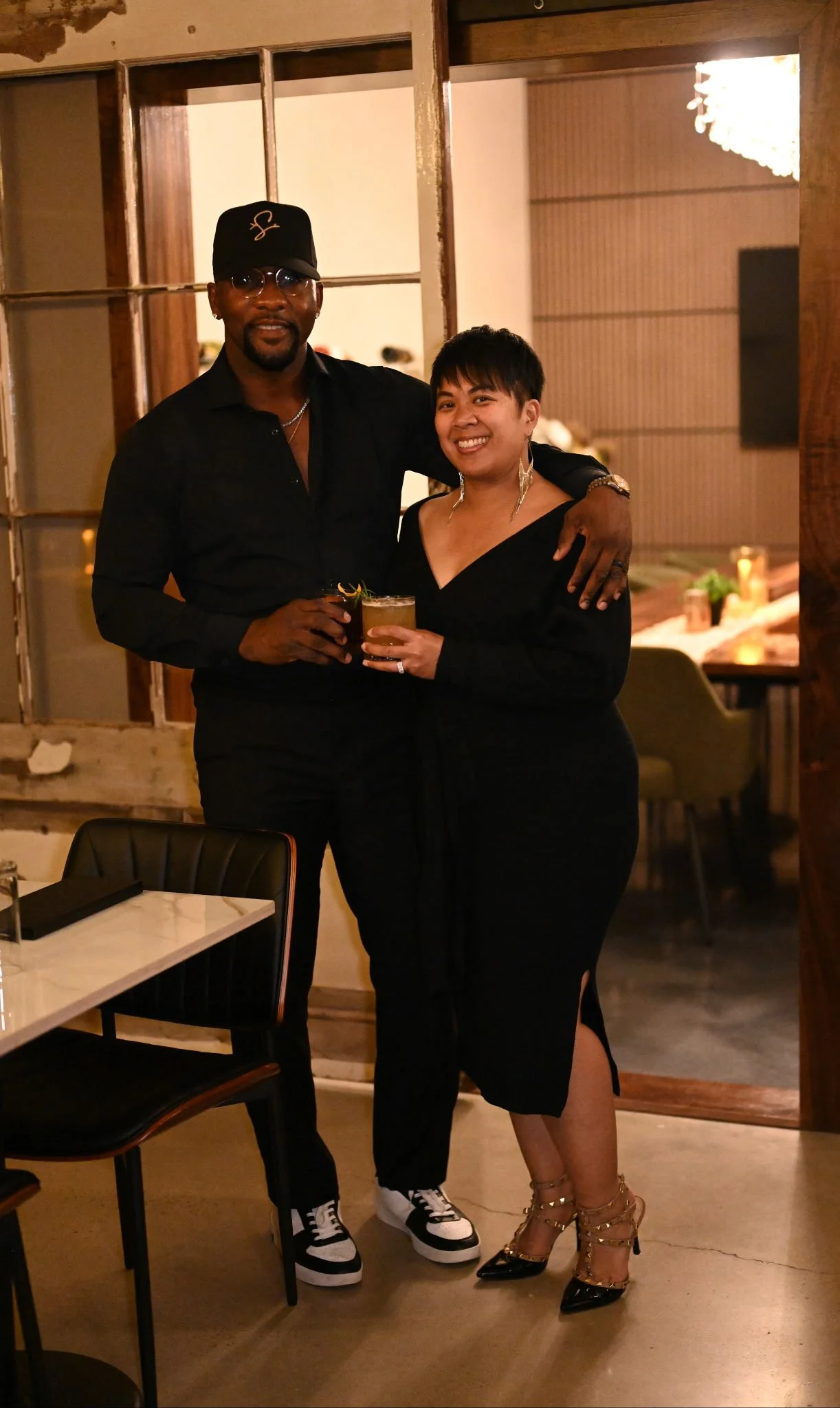 The owners of Sticks-N-Stones cocktail bar and restaurant standing together, holding drinks and smiling.