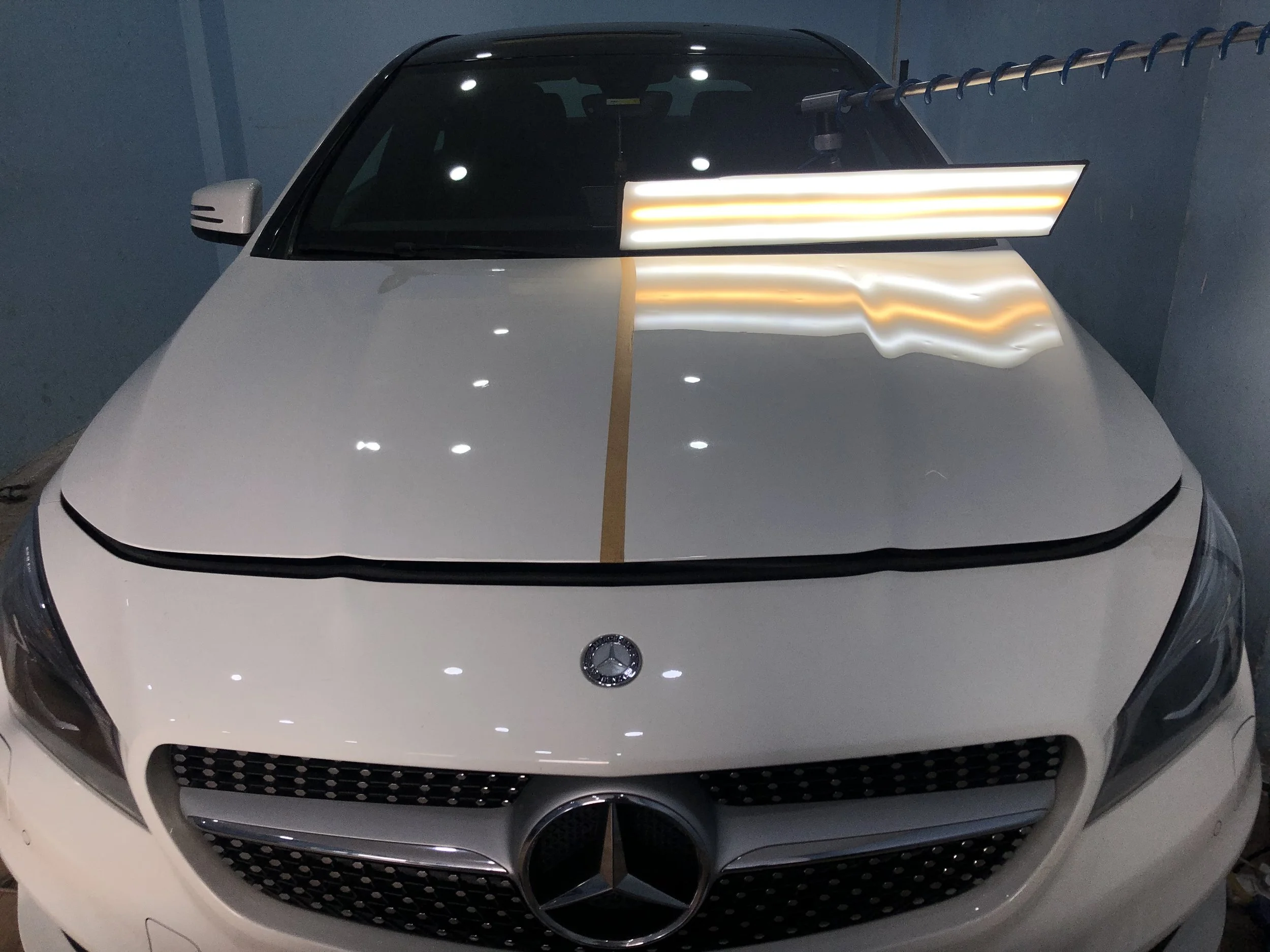 White car undergoing dent repair with a reflection board, focusing on the hood, in a garage setting.