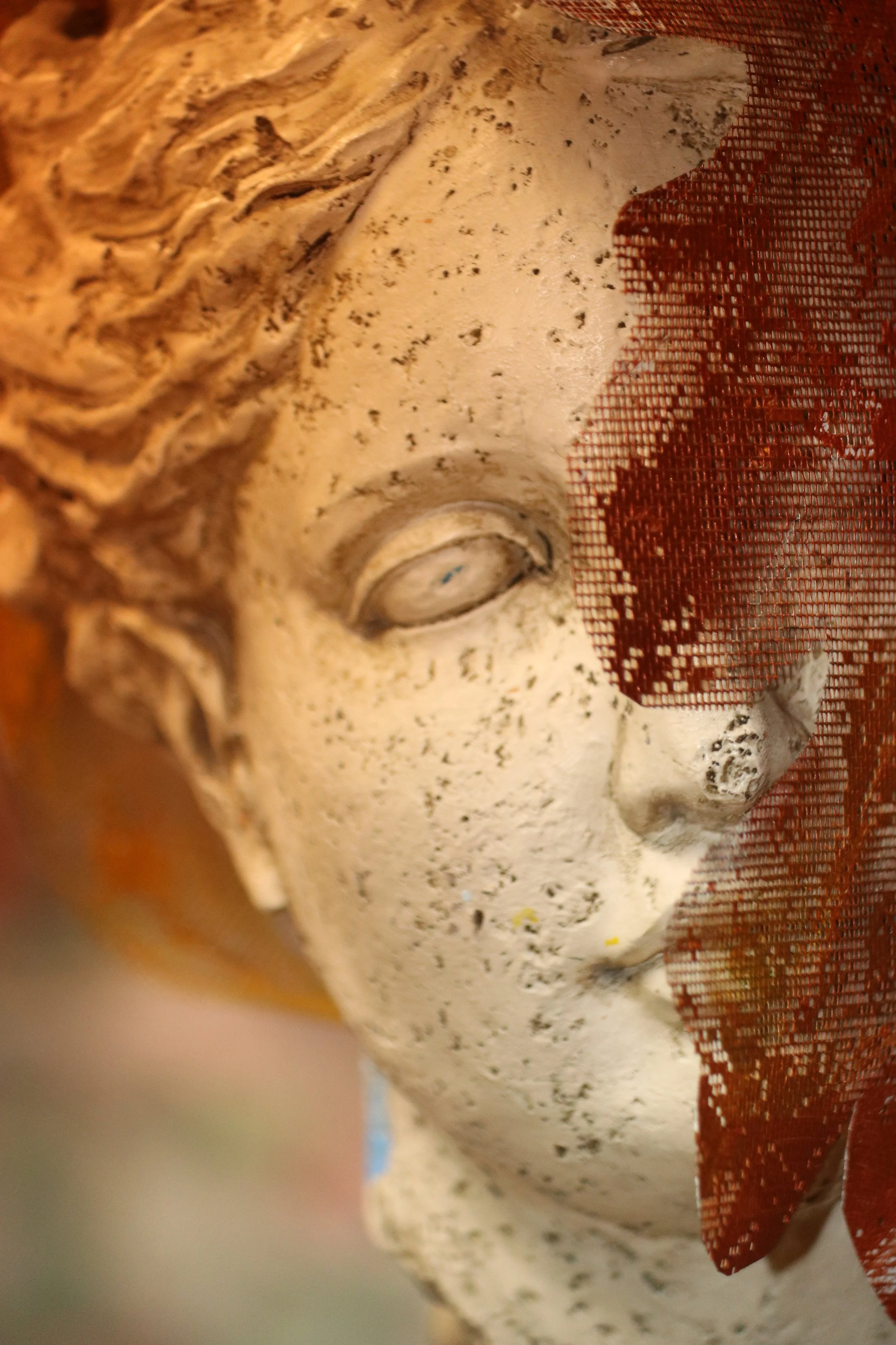 Close-up of a weathered sculpture of a woman's face partially covered by a red mesh fabric.