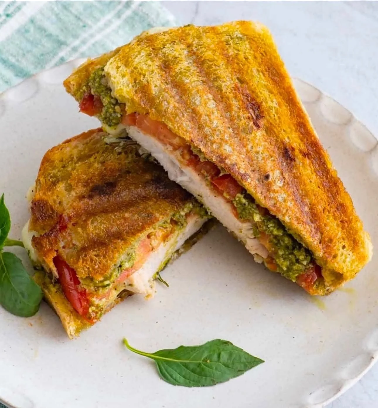 Grilled chicken pesto sandwich with tomatoes and basil on a plate.