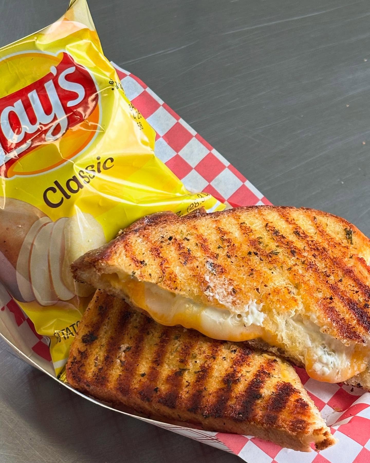 Grilled cheese sandwich with Lay's Classic chips on a checkered paper tray.