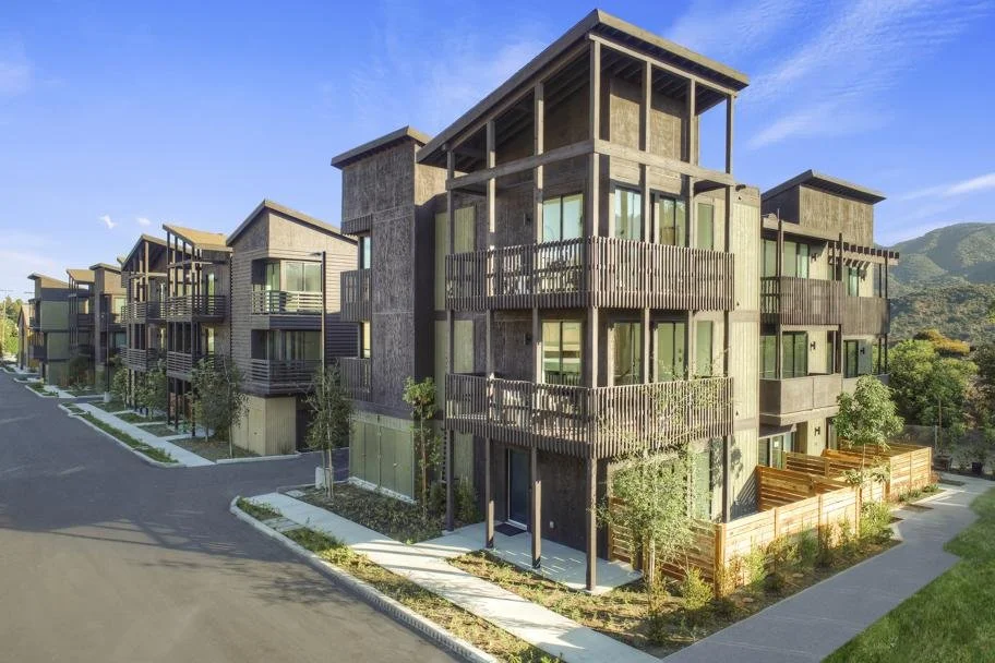 Modern multi-story residential buildings with balconies, large windows, and landscaped surroundings under a clear blue sky.
