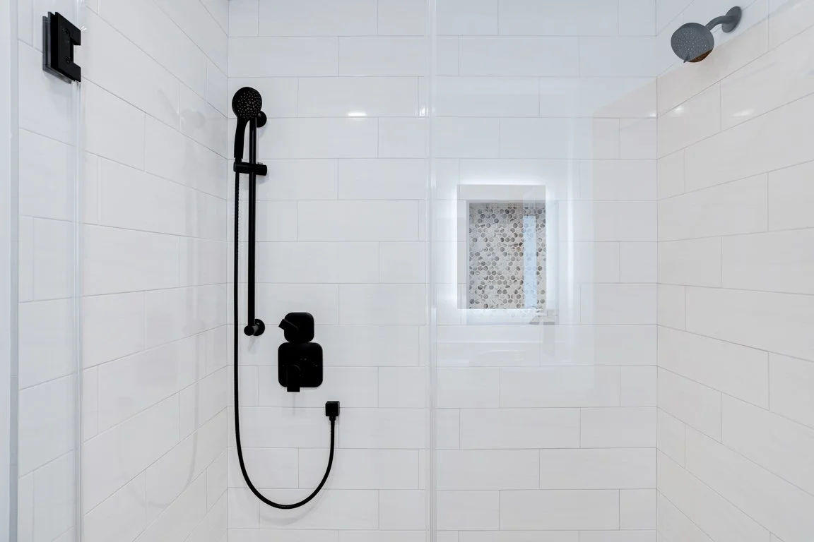 Modern shower with black fixtures, a handheld showerhead, and a small window with pebble tile detail.