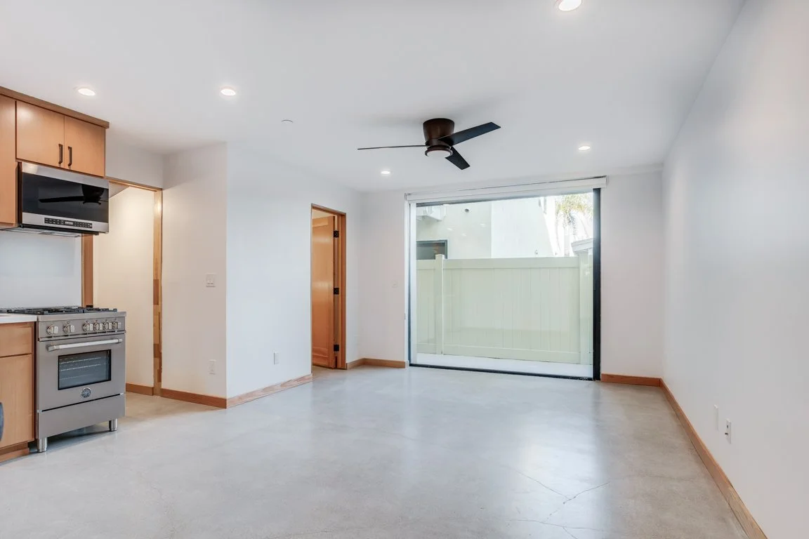Empty living room with a sliding glass door, ceiling fan, and kitchen with stove and microwave