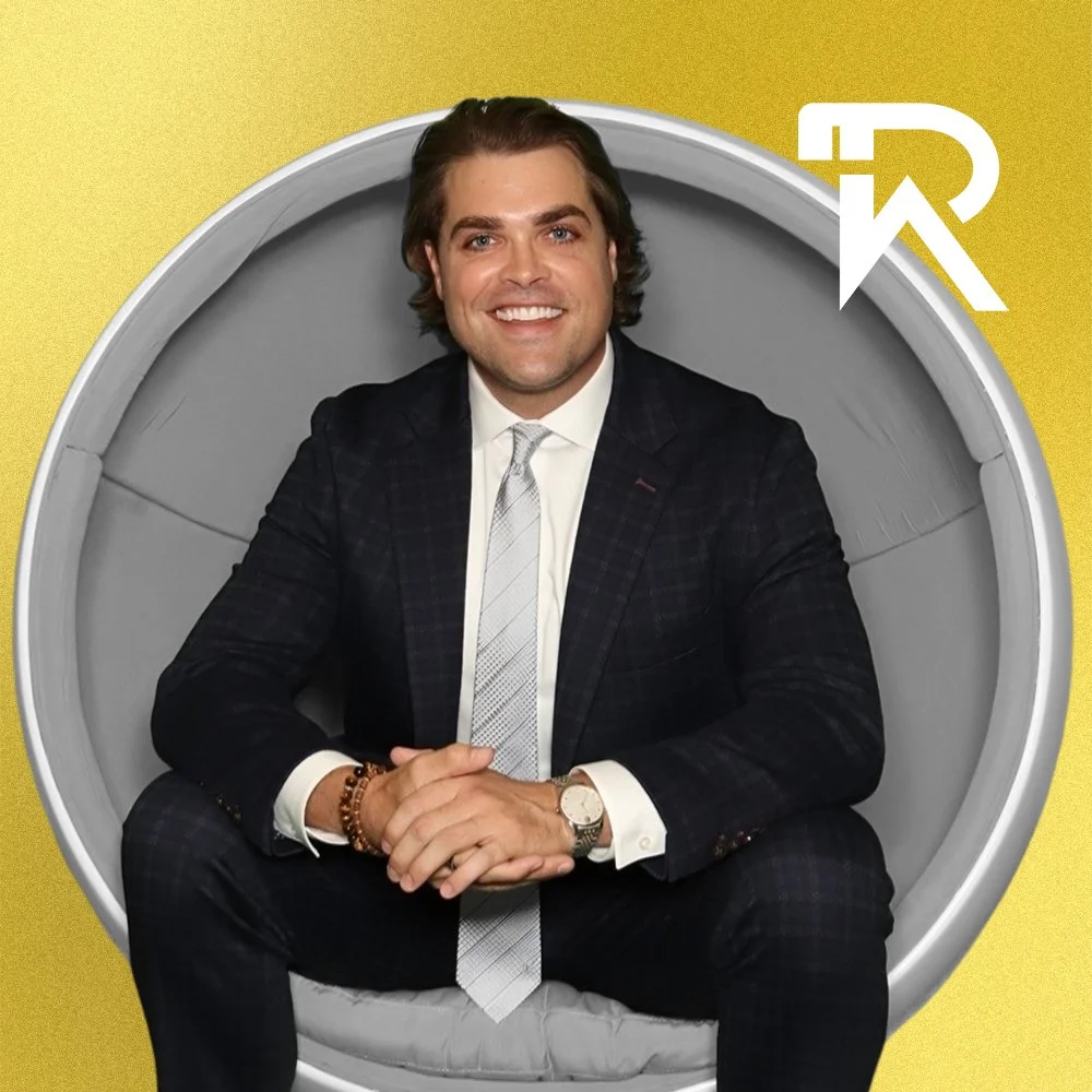 Black and white photo of a smiling man with wavy hair, wearing a quilted jacket, against a solid yellow background with a white logo in the top right corner.