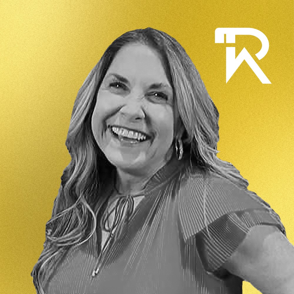 Black and white photo of a smiling woman with wavy hair, wearing a dark top, against a yellow background with a white logo in the upper right corner.