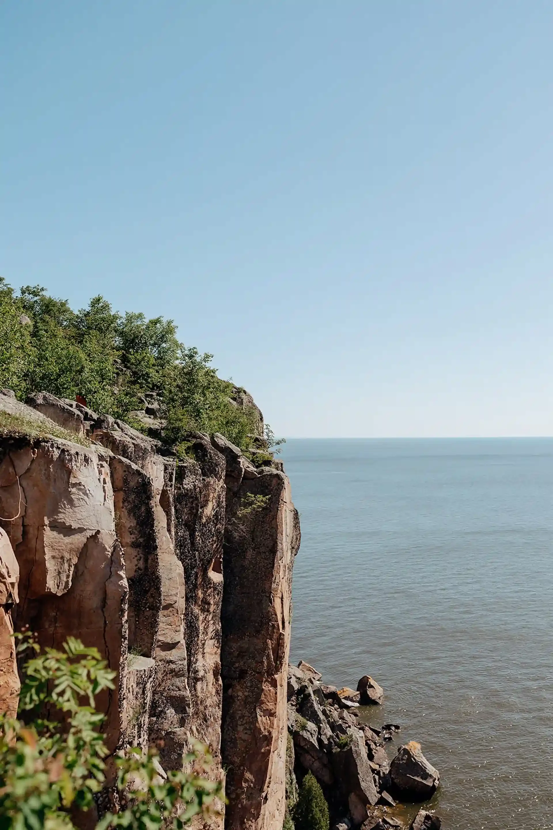 Cliff with trees overlooking a calm sea under a clear blue sky.