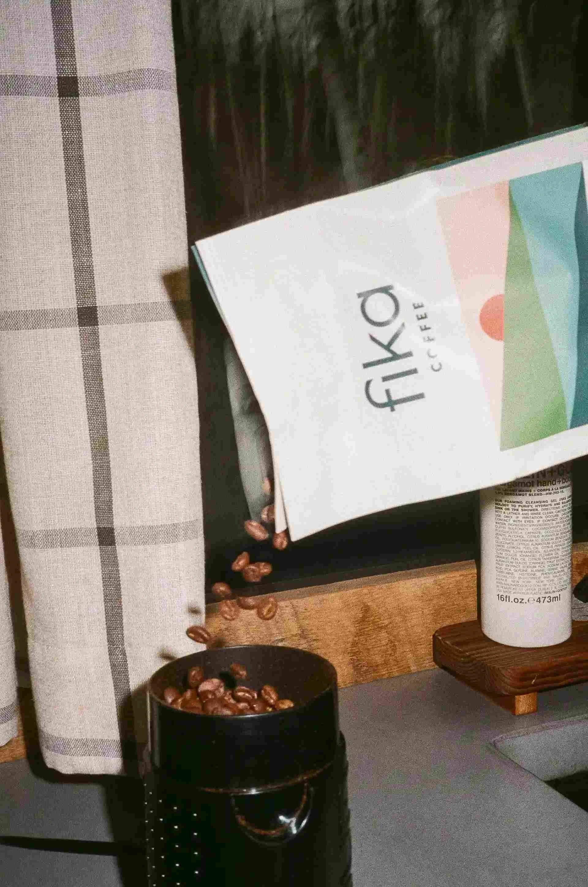 Coffee beans pouring from a bag labeled 'fika coffee' into a black grinder on a countertop.
