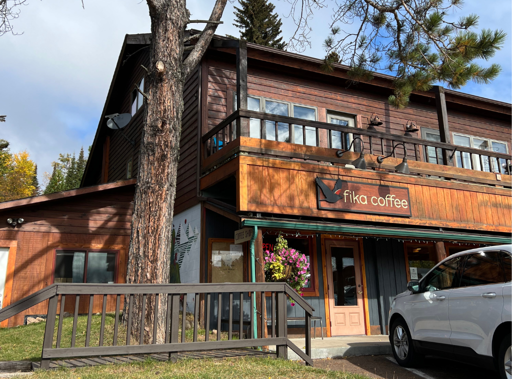 Exterior of a wooden coffee shop named Fika Coffee, surrounded by trees, with a parked white car in front.