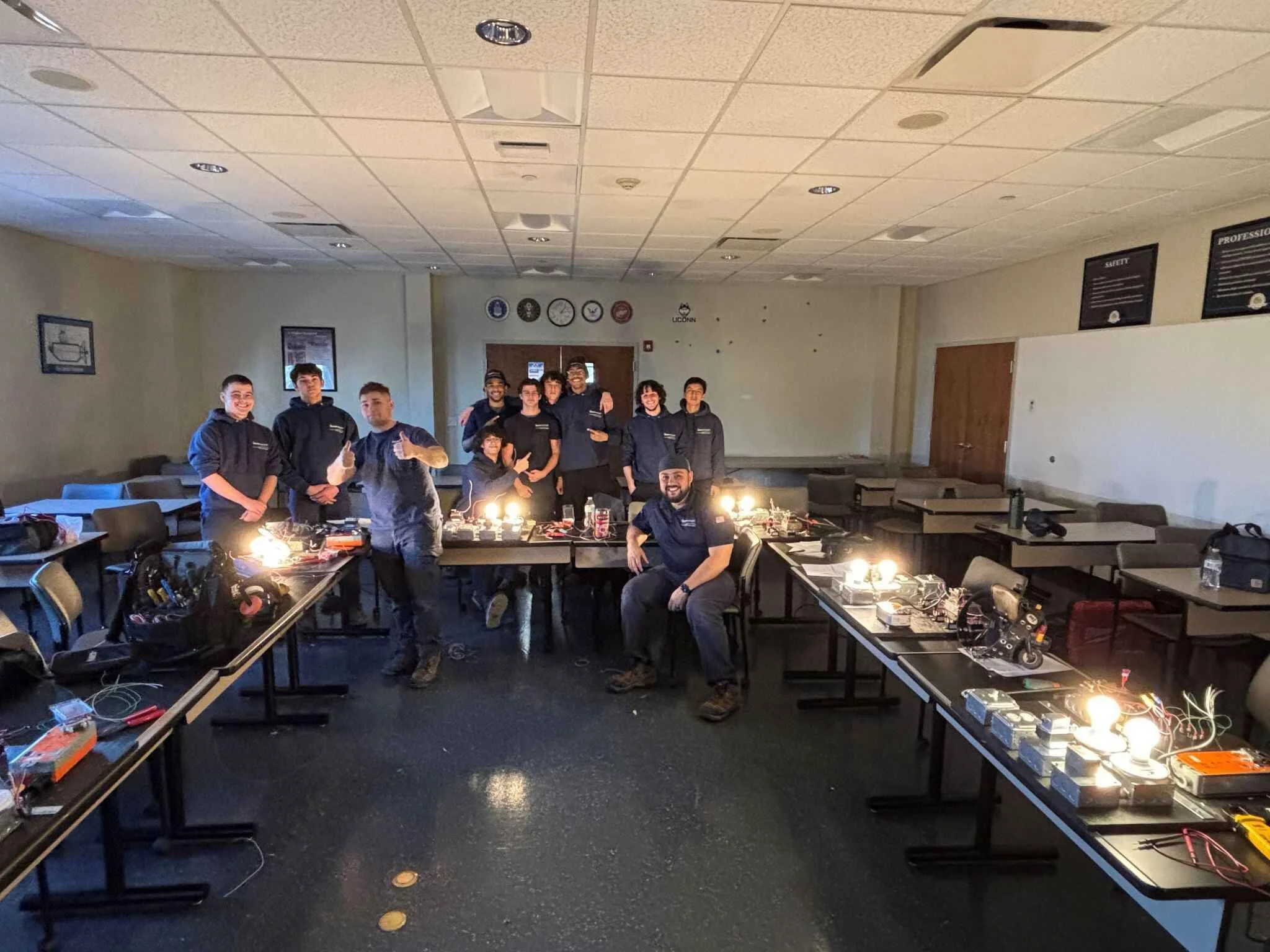 Group of people in a classroom with electronic equipment and working lights, posing for a photo.