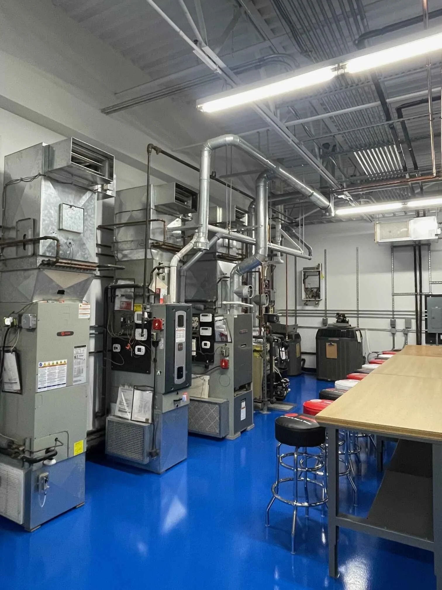 Industrial room with metallic equipment, pipes, and control panels on a shiny blue floor, with high ceilings and overhead fluorescent lighting.