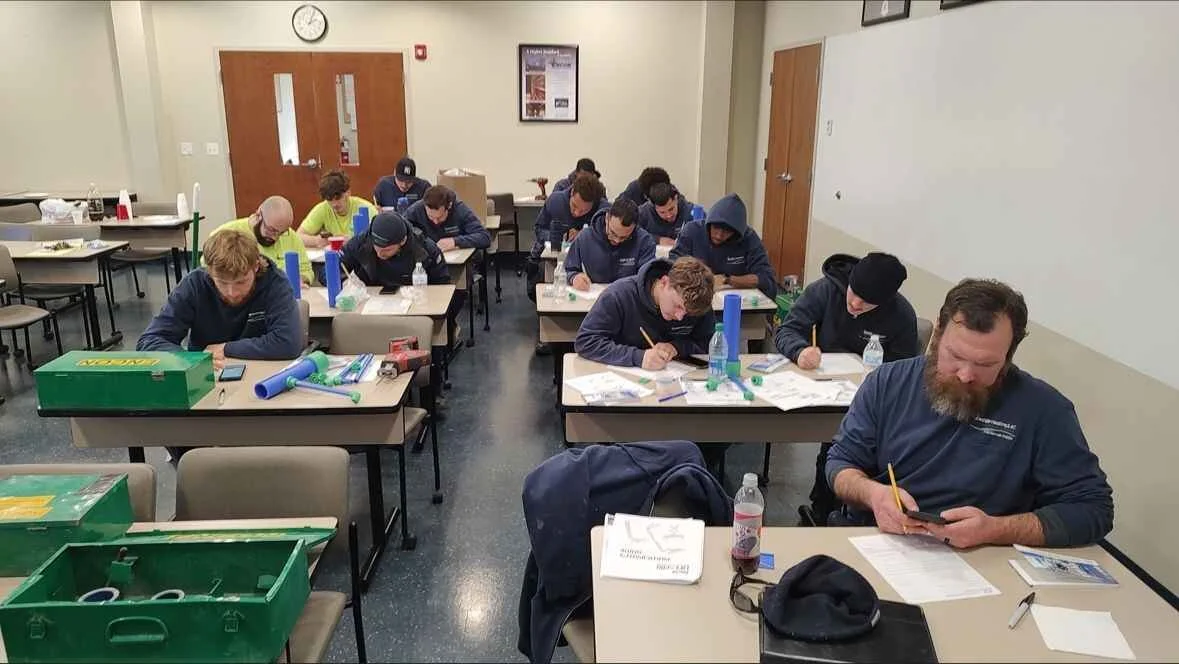 Group of students and instructor seated at desks in a classroom, working on papers and using devices.