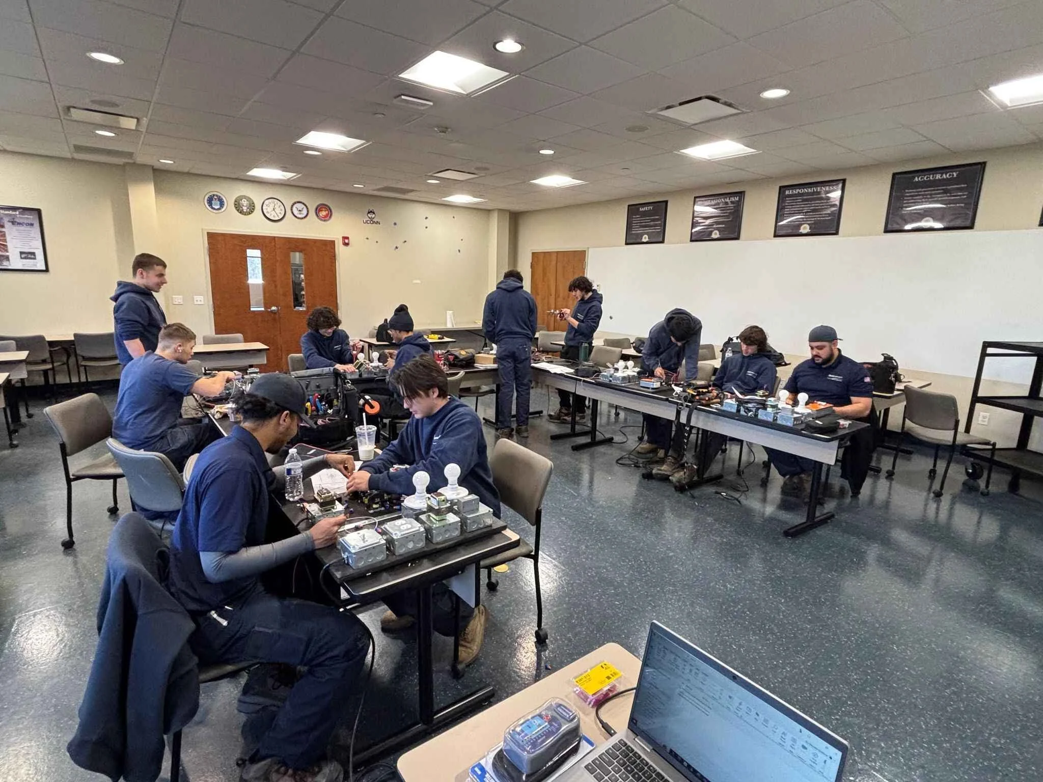 Group of people working on electronic projects at tables in a classroom or workshop setting