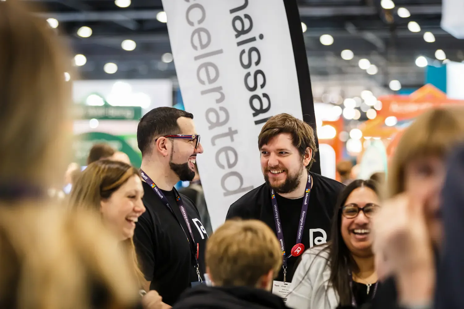 Group of smiling people at a professional event, wearing lanyards, standing near a banner that says 'Raised Calendar' with a busy, well-lit background.