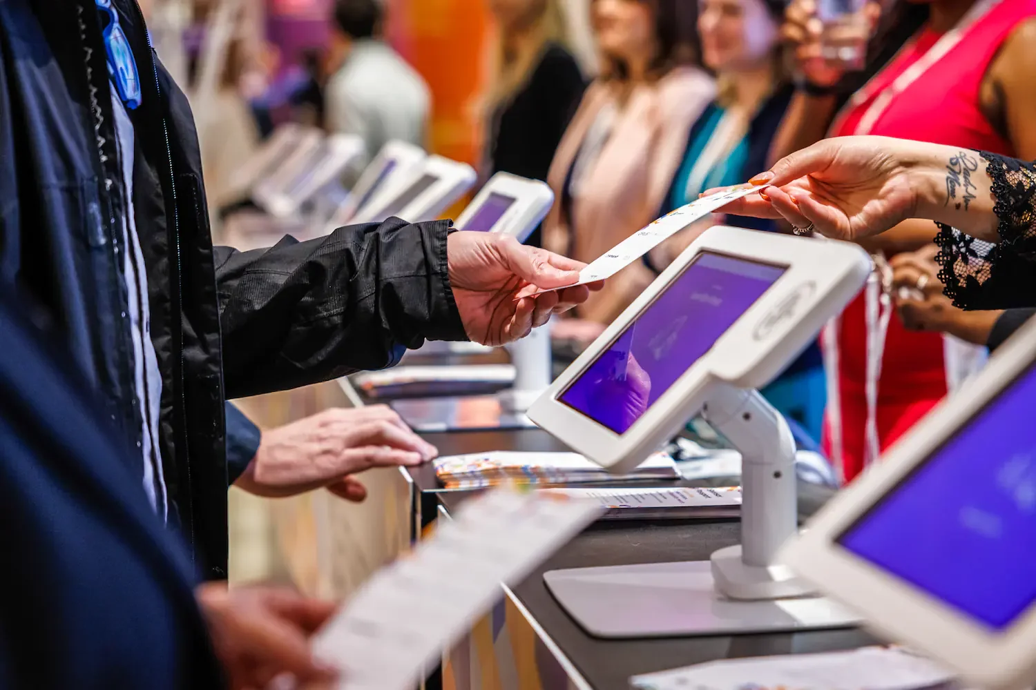 People at a checkout counter using touchscreen point-of-sale systems to pay for items, with cashiers assisting in a busy retail store.