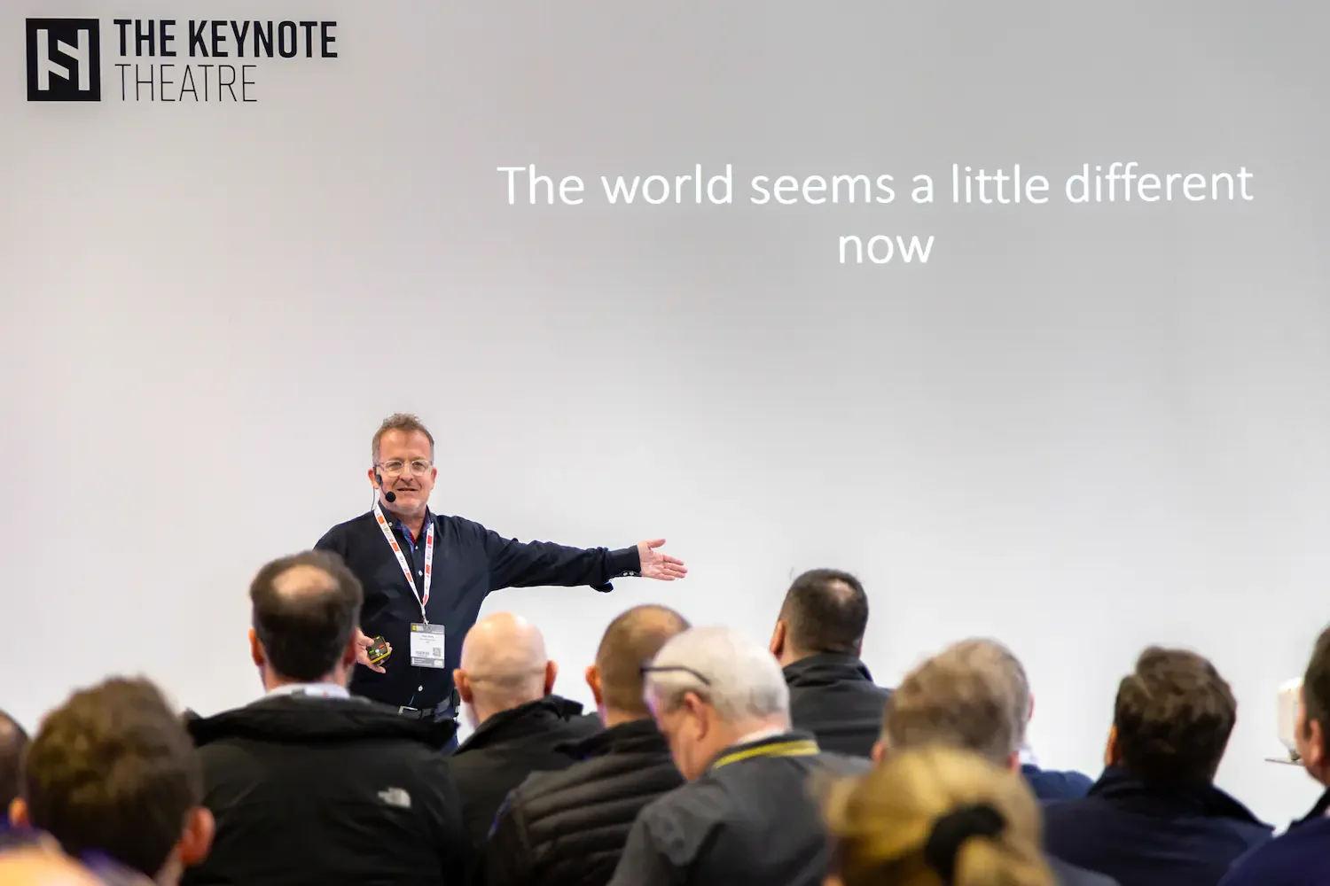 A man giving a presentation at The Keynote Theatre with a slide that reads, 'The world seems a little different now,' in front of an audience.