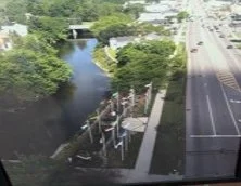 Aerial view of a river running parallel to a road with a line of flags displayed along a walkway.