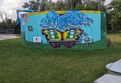 Colorful mural on a curved wall with a butterfly and various abstract designs in a grassy area.