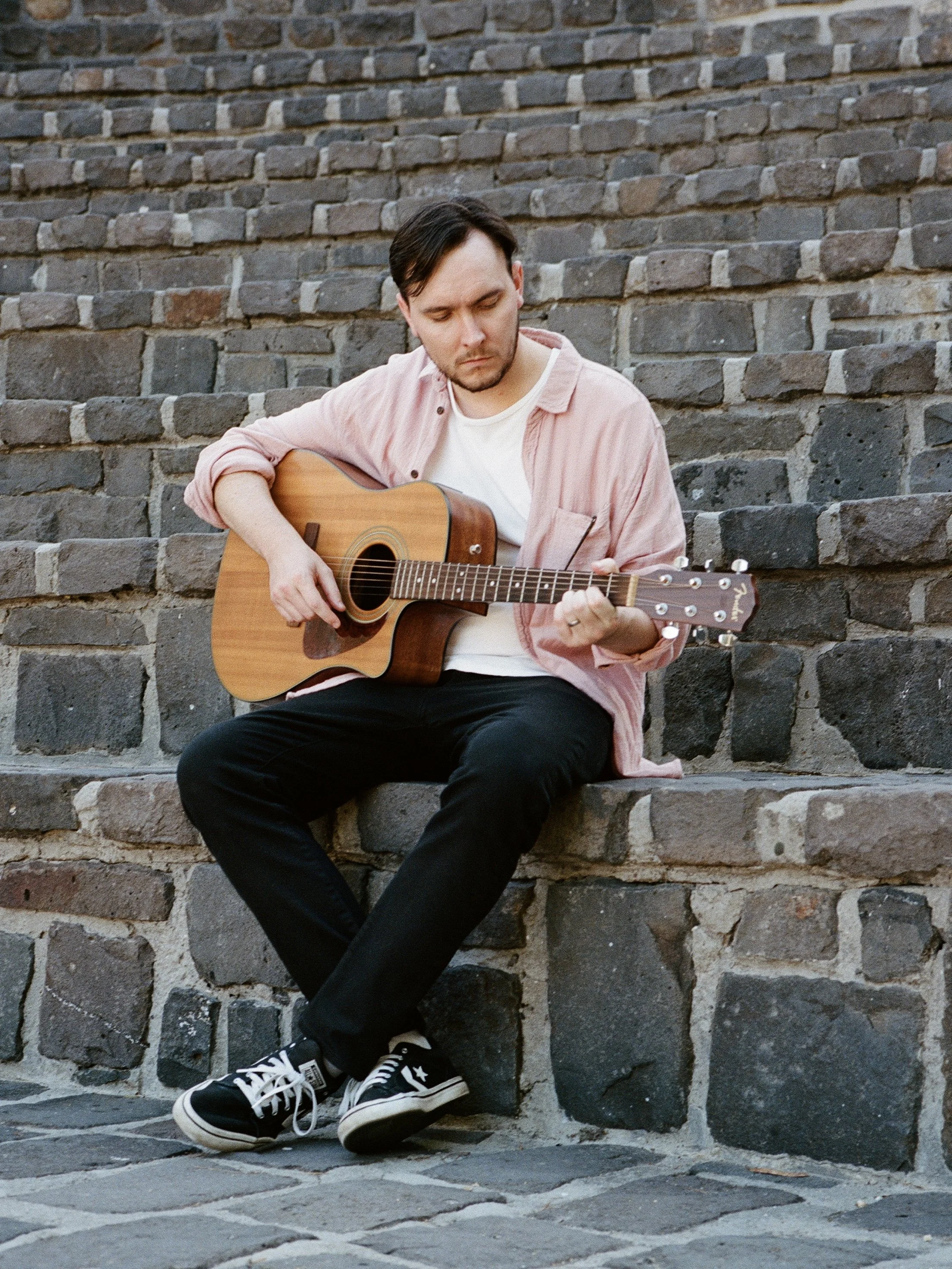 Jord. sits on cobblestone steps playing his guitar.