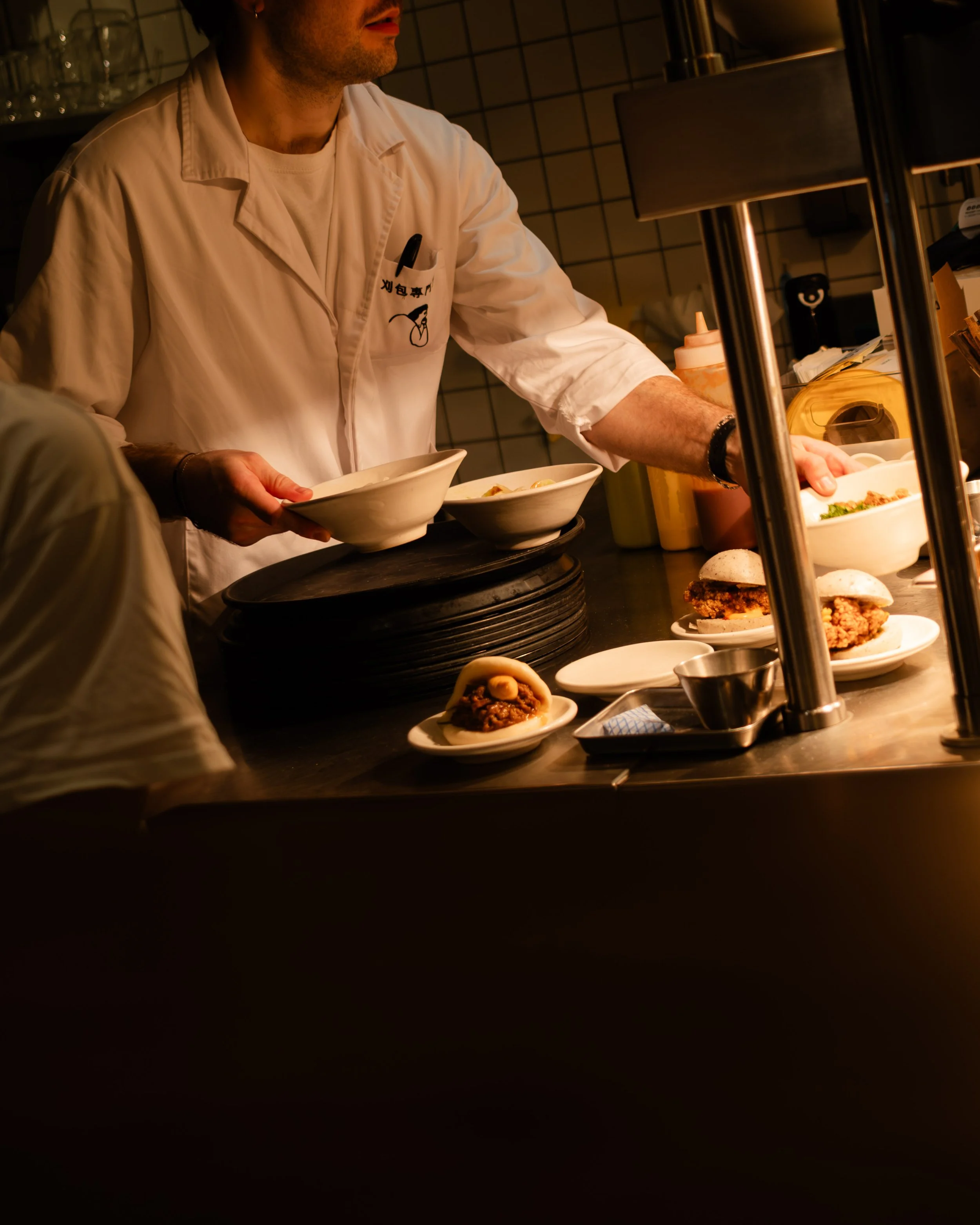 A chef preparing food behind a counter with plates of burgers and bowls, with condiments and kitchen utensils visible. Lionel Chu - Hotel & Travel Photographer
