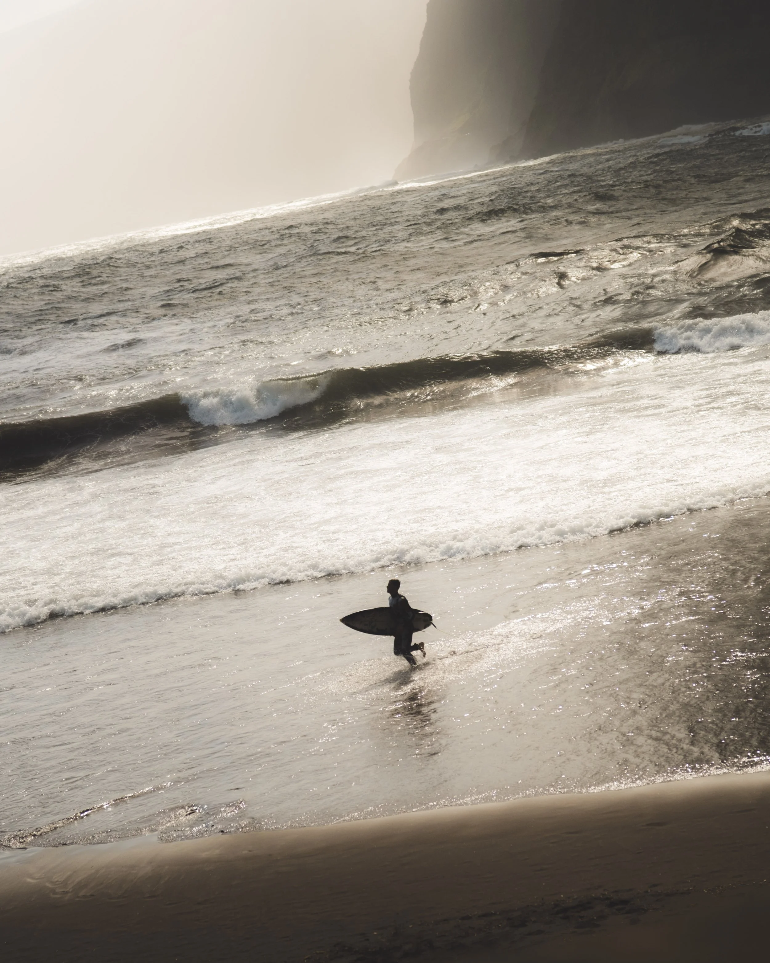 A person holding a surfboard and running on the beach near the ocean waves during sunset.