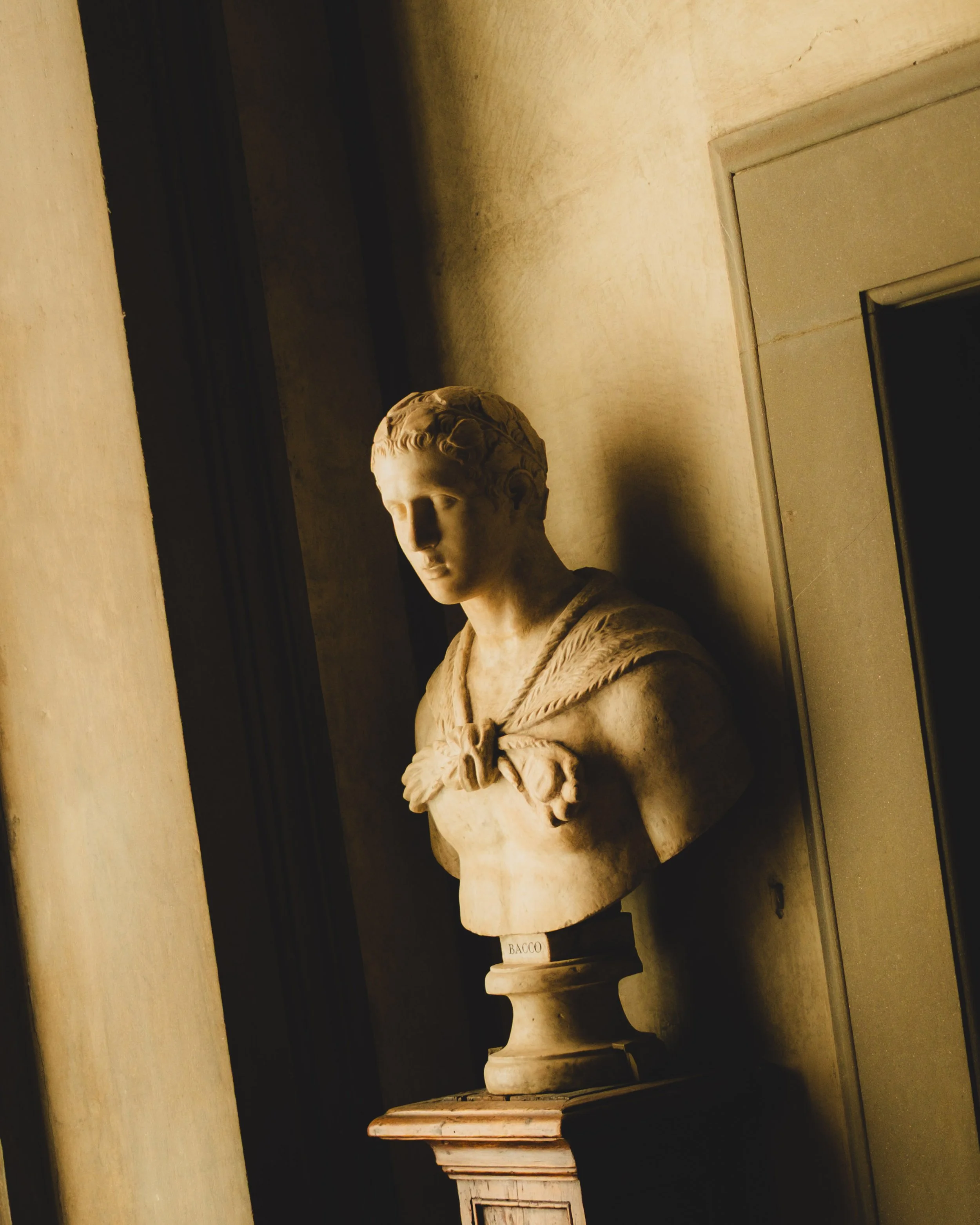 Marble bust sculpture of a young man with curly hair, wearing a sailor's or naval uniform, on a pedestal in a museum setting. Lionel Chu - Hotel & Travel Photographer