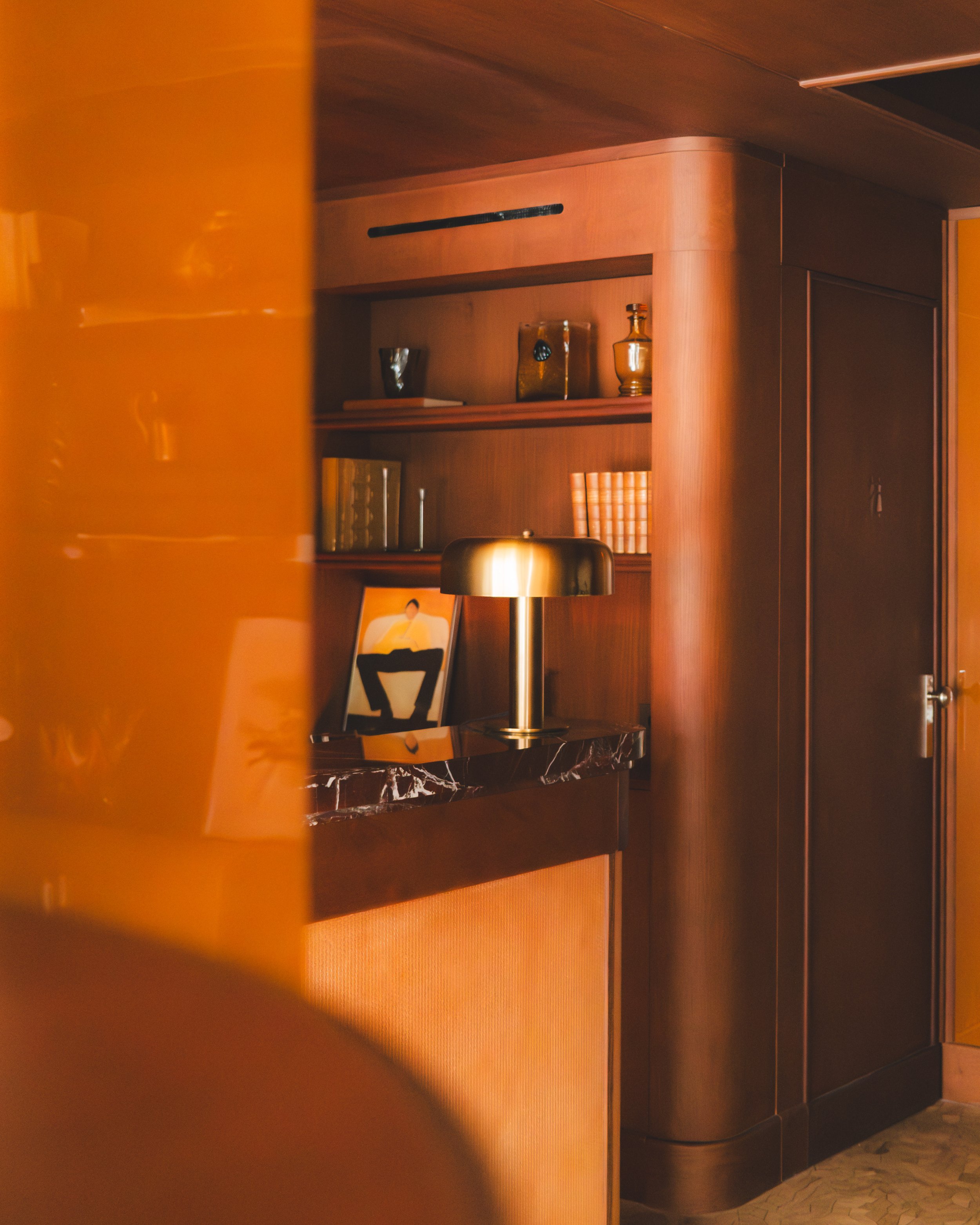 A room with wooden walls and shelves, displaying various decorative vases. There is a lamp with a brass finish on a shelf, and a chair with a artistic backrest. The corner of the room has a closed door.