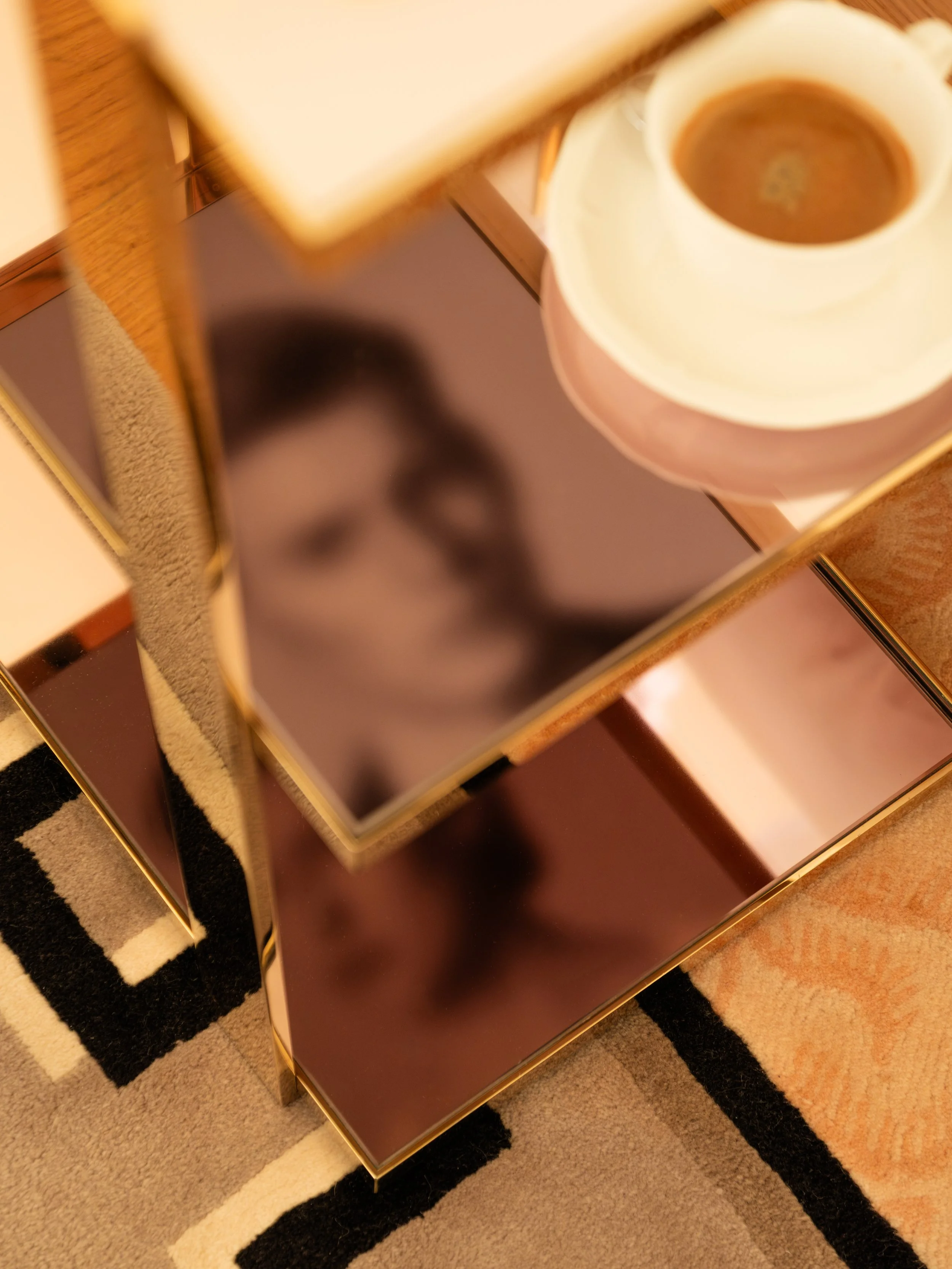 A mirrored side table with a cup of coffee and a reflection of a person's face. Lionel Chu - Hotel & Travel Photography