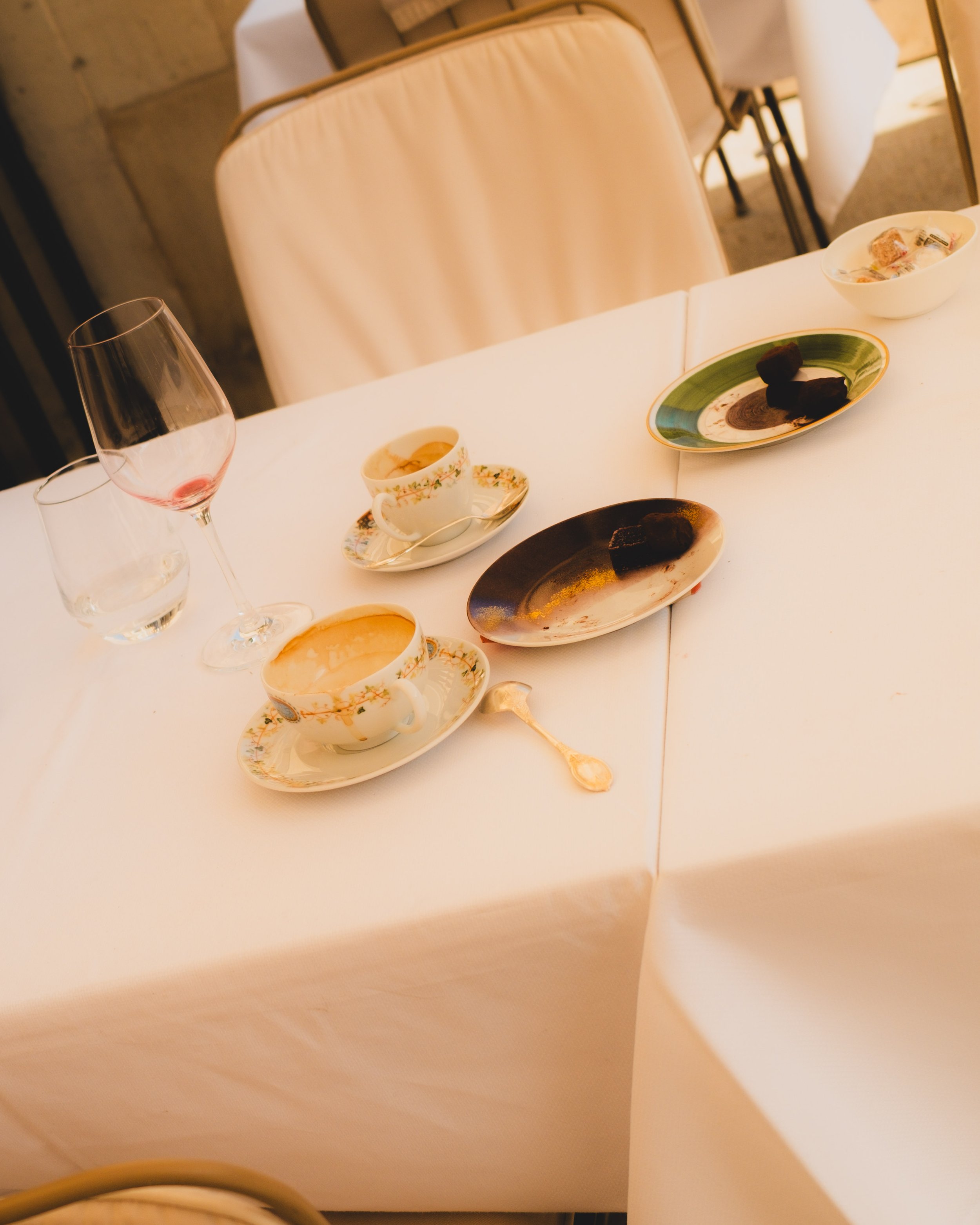Table with empty teacups, dessert plates, wine glass, and water glass on a white tablecloth. Lionel Chu - Hotel & Travel Photographer.