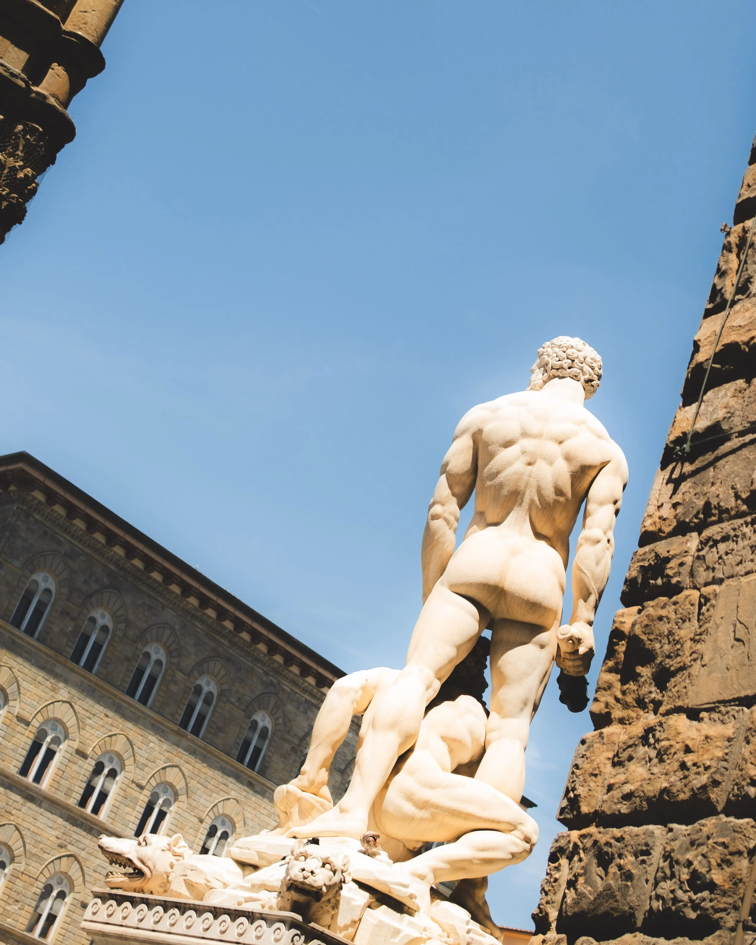 Marble statue of a muscular male figure seen from behind, outdoors with a historic building in the background. Lionel Chu - Hotel & Travel Photographer