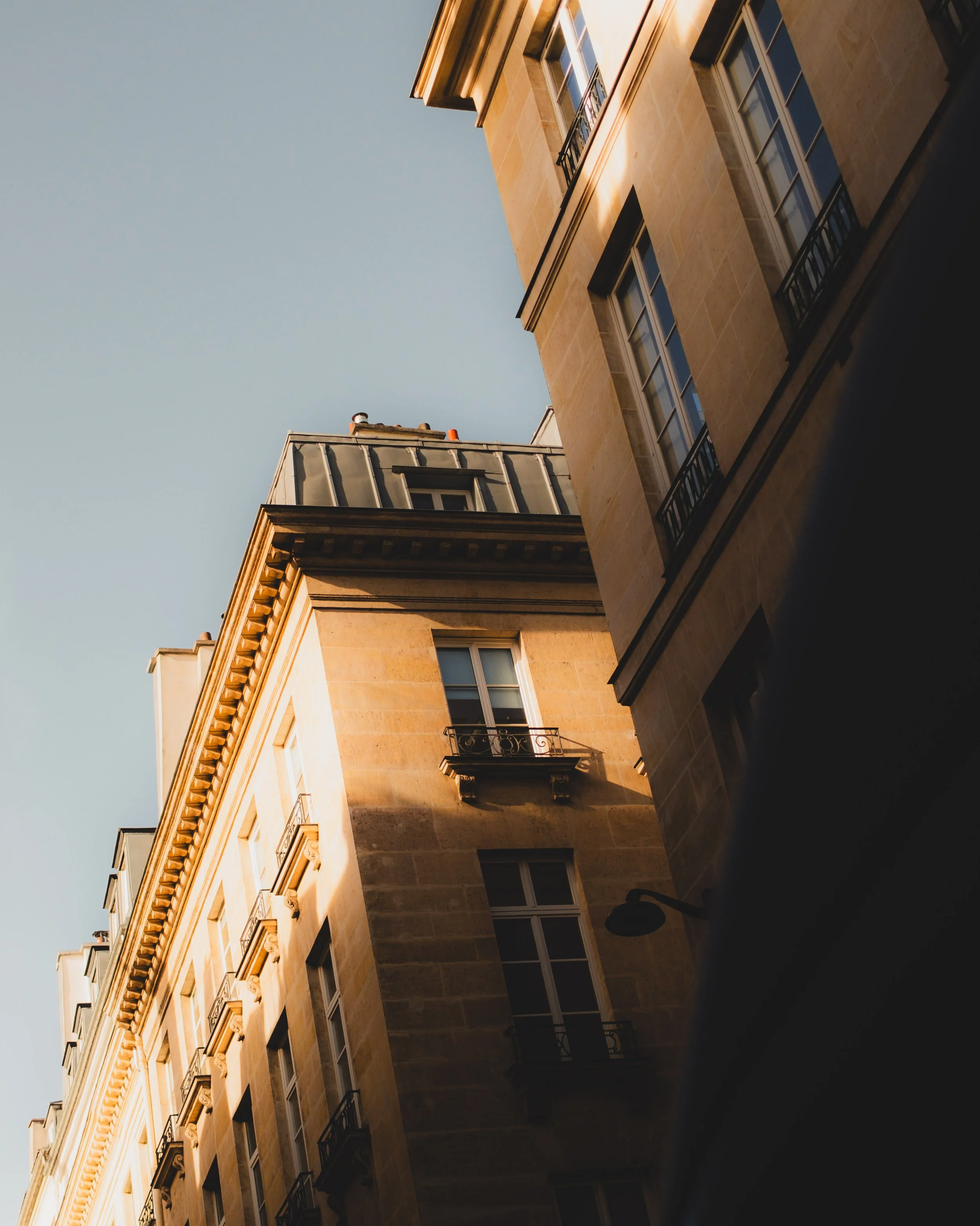 View of a European-style building from below, displaying windows with small balconies and decorative architectural details, with a clear sky in the background. Lionel Chu - Hotel & Travel Photographer