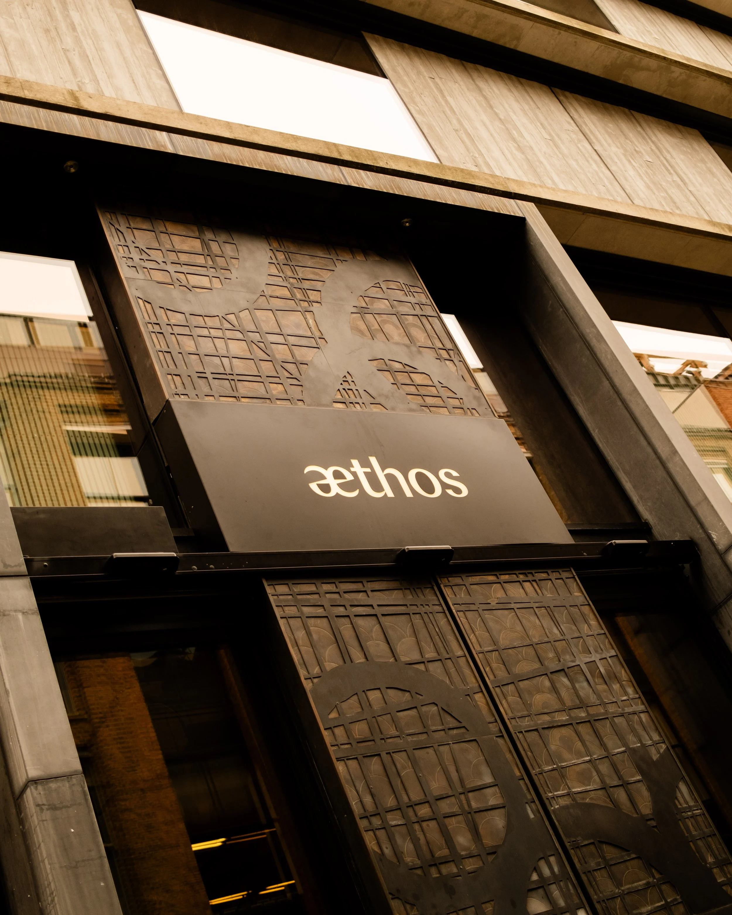 Close-up of a hotel's entrance with a sign that says 'Aethos' and decorative metalwork panels on the doorway. Lionel Chu - Hotel & Travel Photographer
