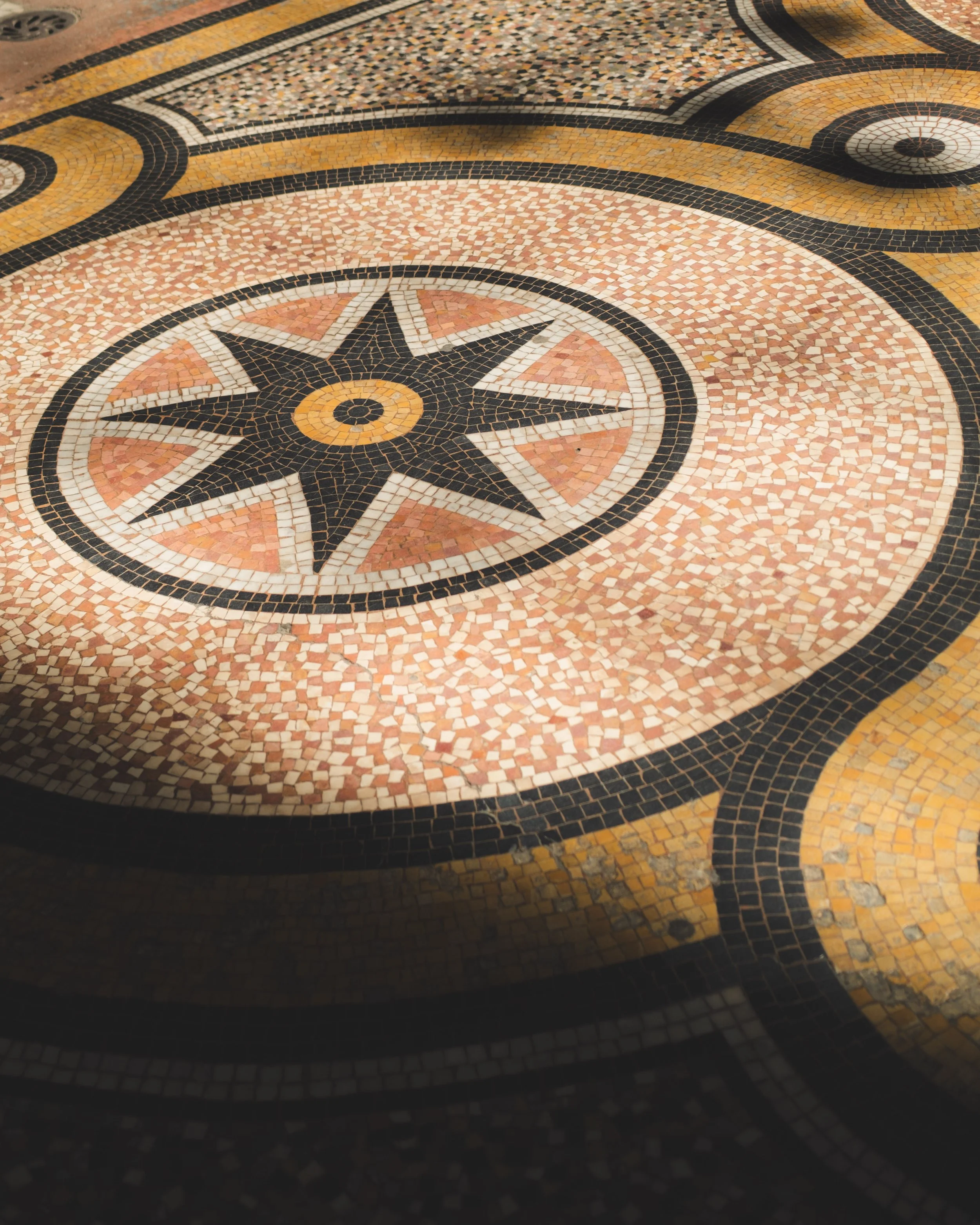 Close-up of a decorative mosaic floor with a compass rose design and black, white, yellow, and pink tiles.