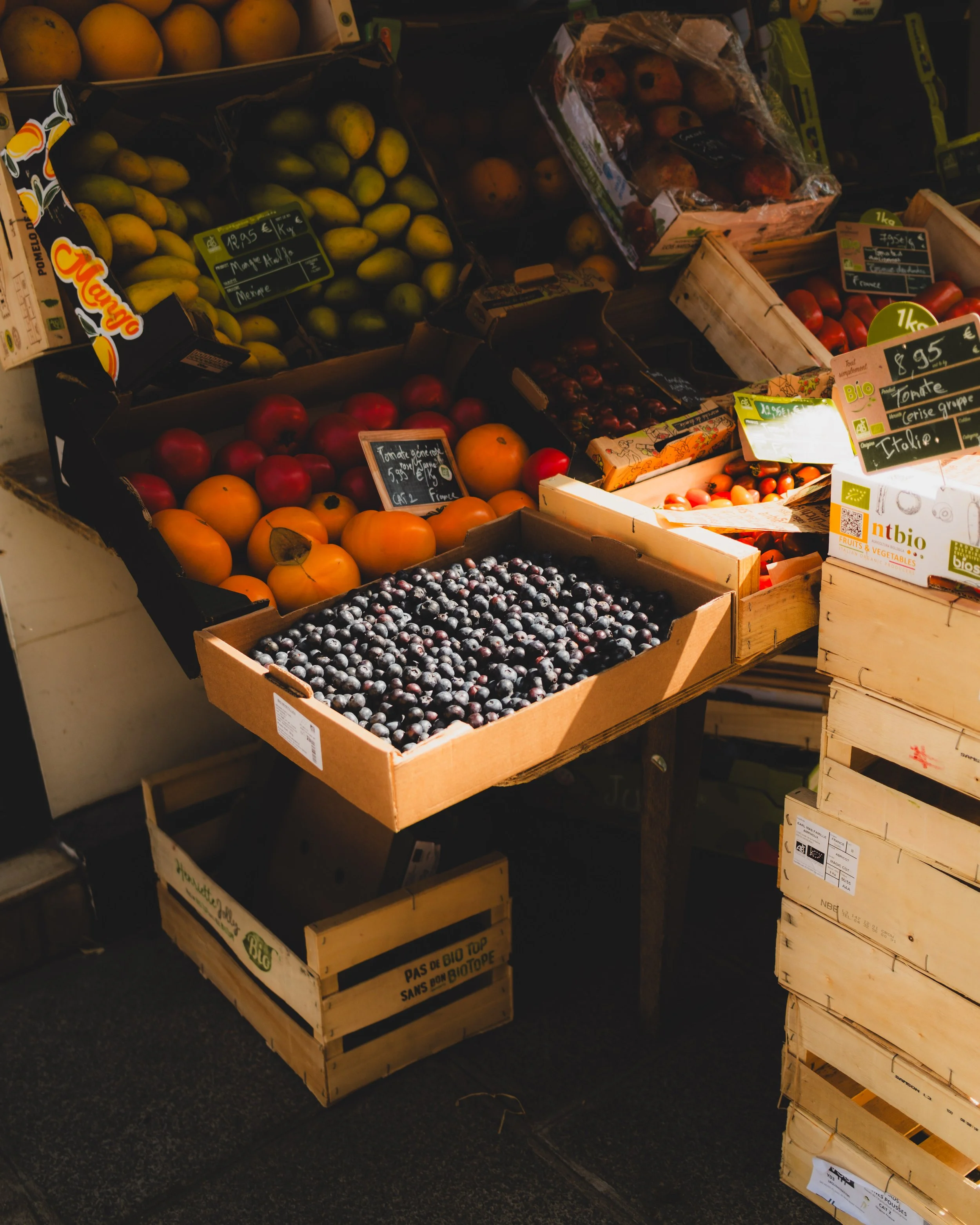 Various fresh fruits including blueberries, tomatoes, peaches, and apples displayed in boxes at a market. Lionel Chu - Hotel & Travel Photographer