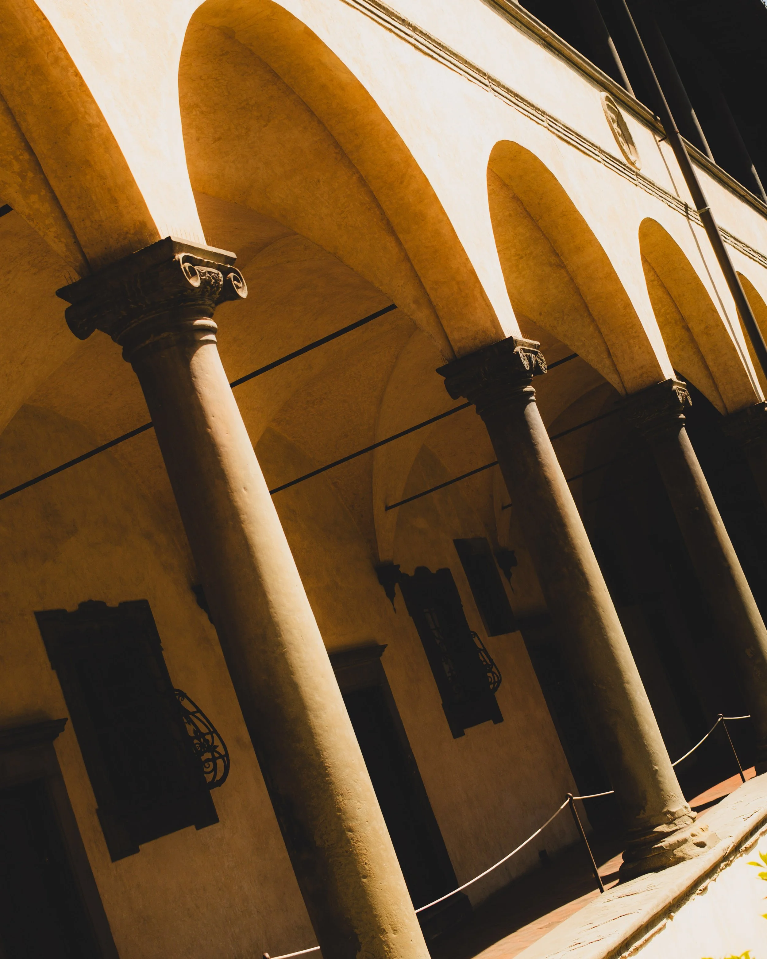 Tuscan-style building with stone columns and arches, beige stucco walls, windows with decorative wrought iron grilles, and a yellow rope barrier outside. Lionel Chu - Hotel & Travel Photographer