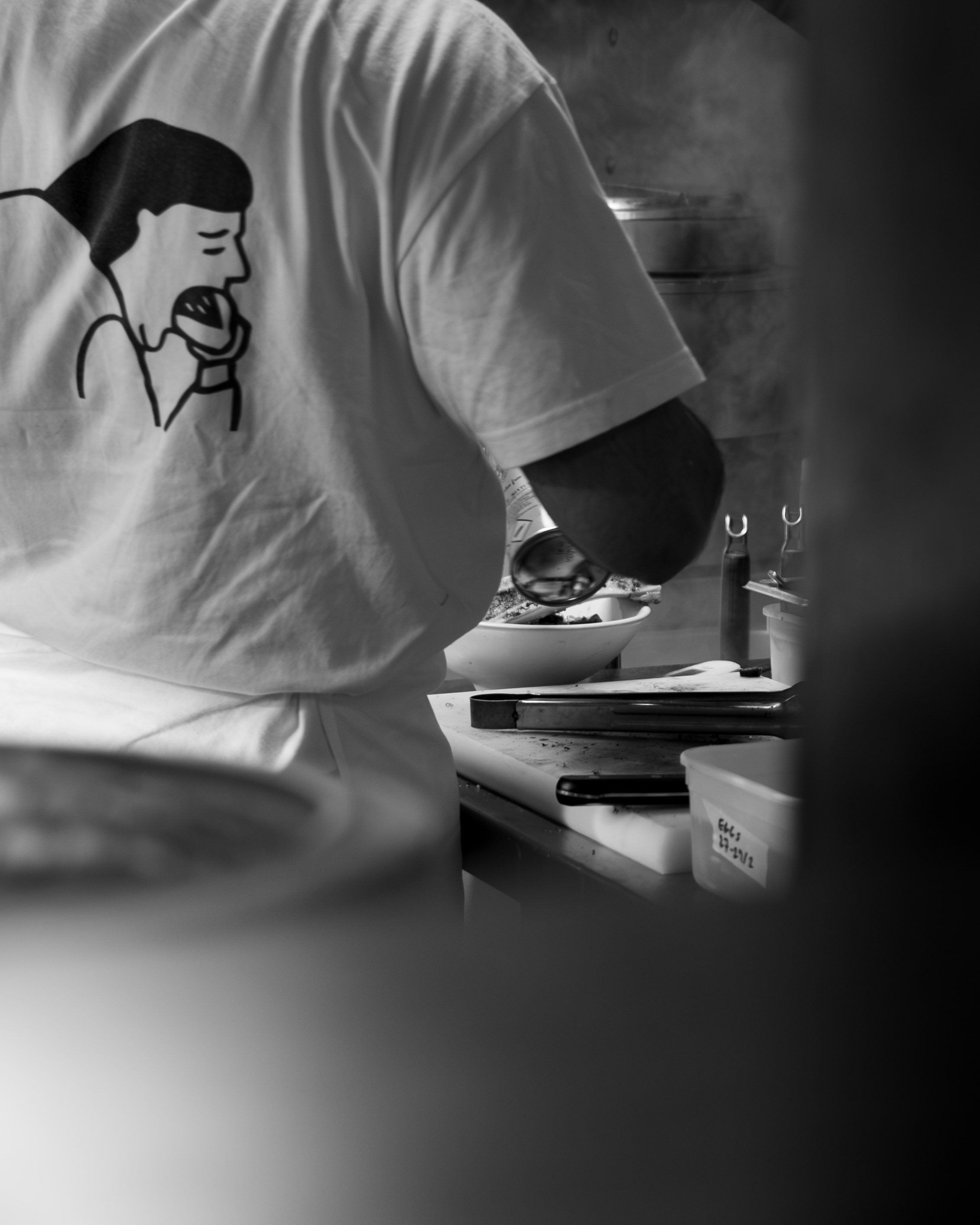 Person wearing a T-shirt with a graphic of a woman screaming into a microphone, working in a kitchen with a bowl and utensils on a countertop. Lionel Chu - Hotel & Travel Photographer