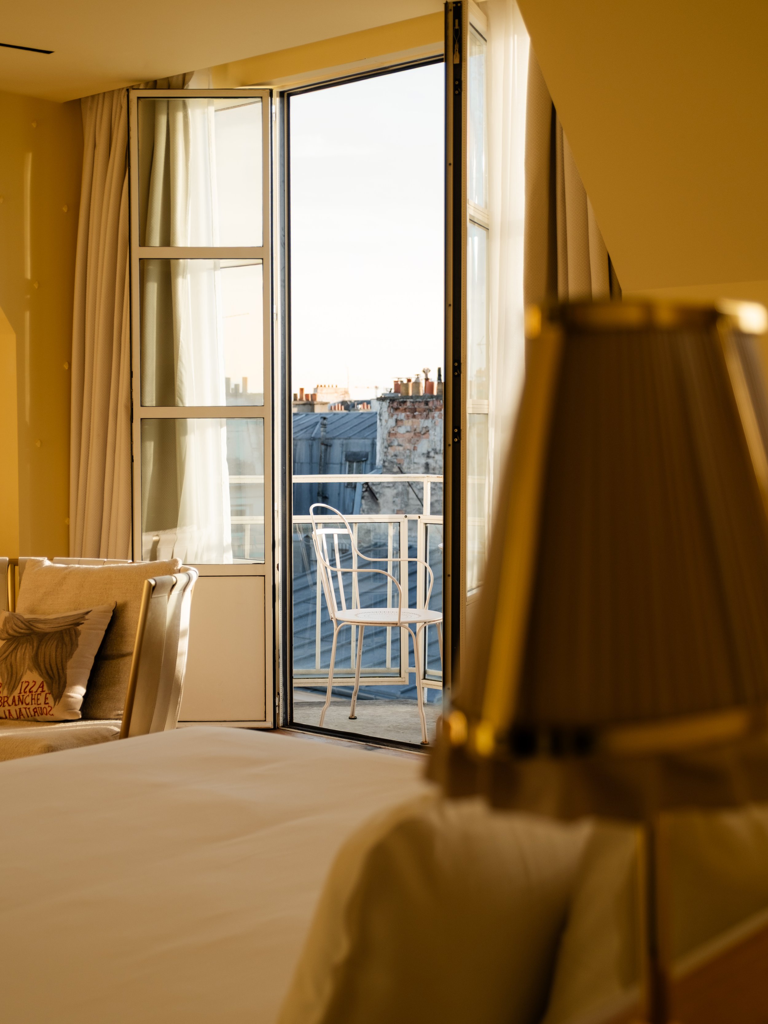 Hotel room with open balcony door, a chair outside on the balcony, and sunlight coming in. Lionel Chu - Hotel & Travel Photography