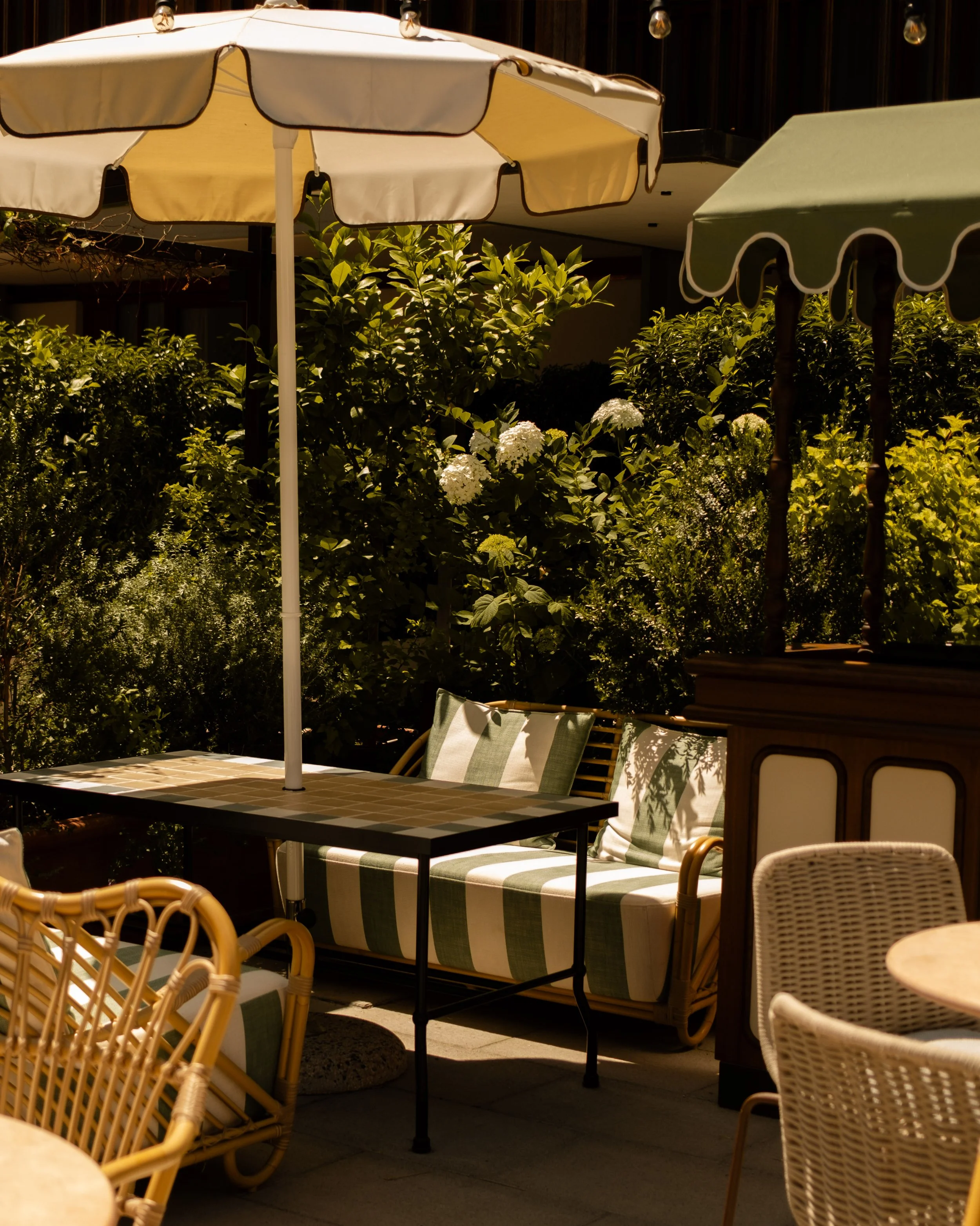 Outdoor patio with striped cushioned seating, umbrellas, and lush greenery. Lionel Chu - Hotel & Travel Photography