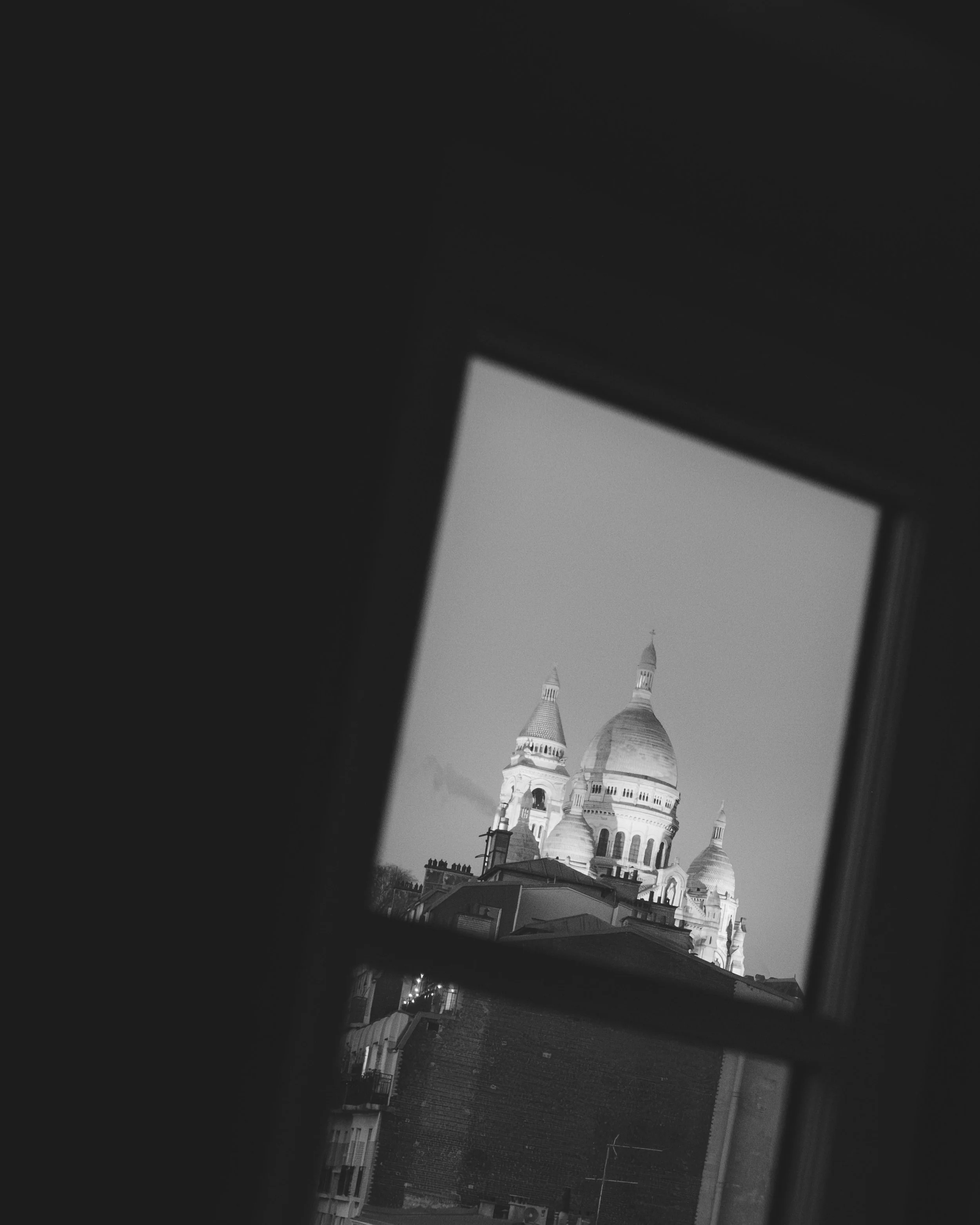 A black and white photo of a religious or historic building with multiple domes and towers seen through a window or mirror, with a dark frame around the edges.
