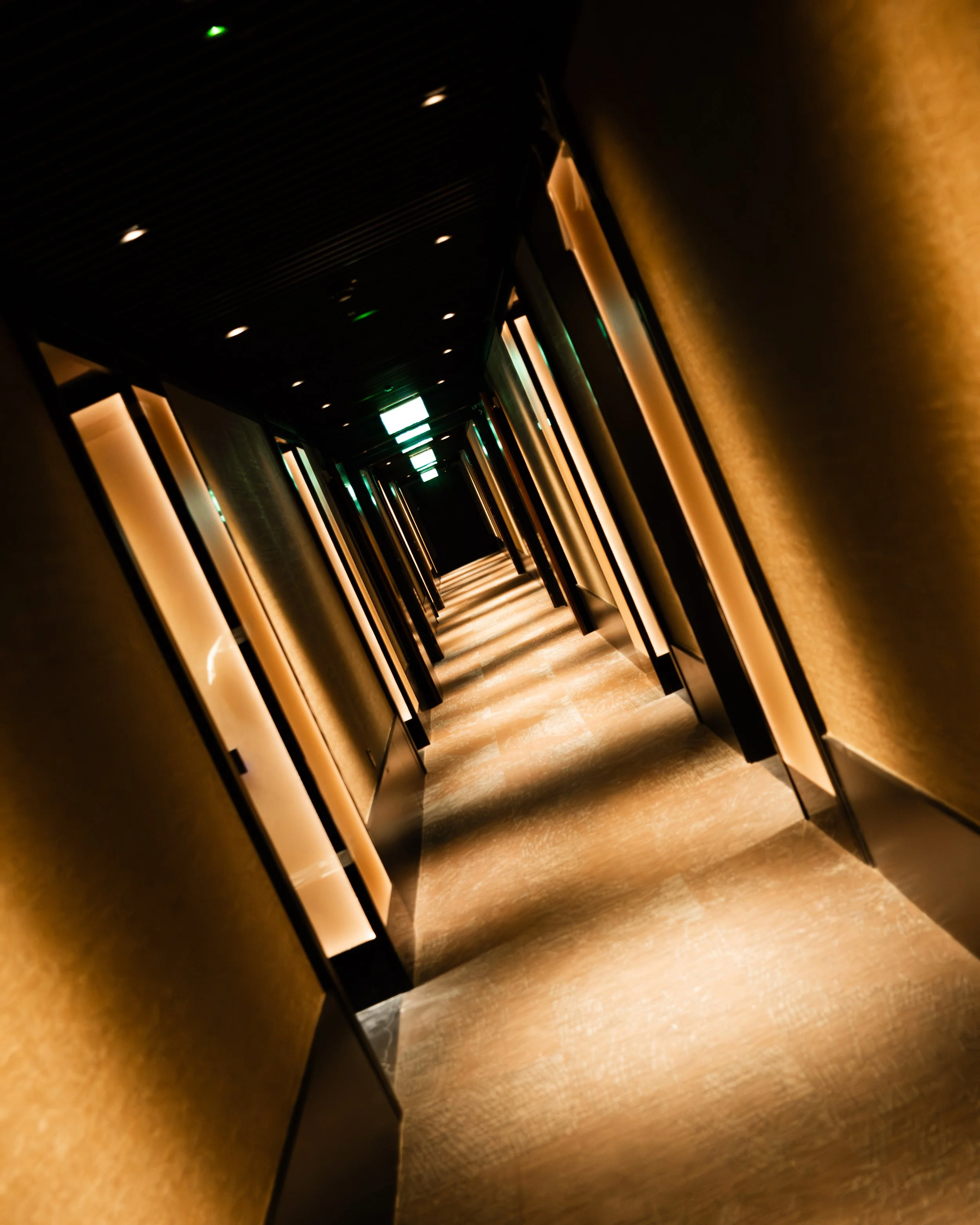 Long hotel corridor with warm lighting and closed doors on both sides. Lionel Chu - Hotel & Travel Photographer
