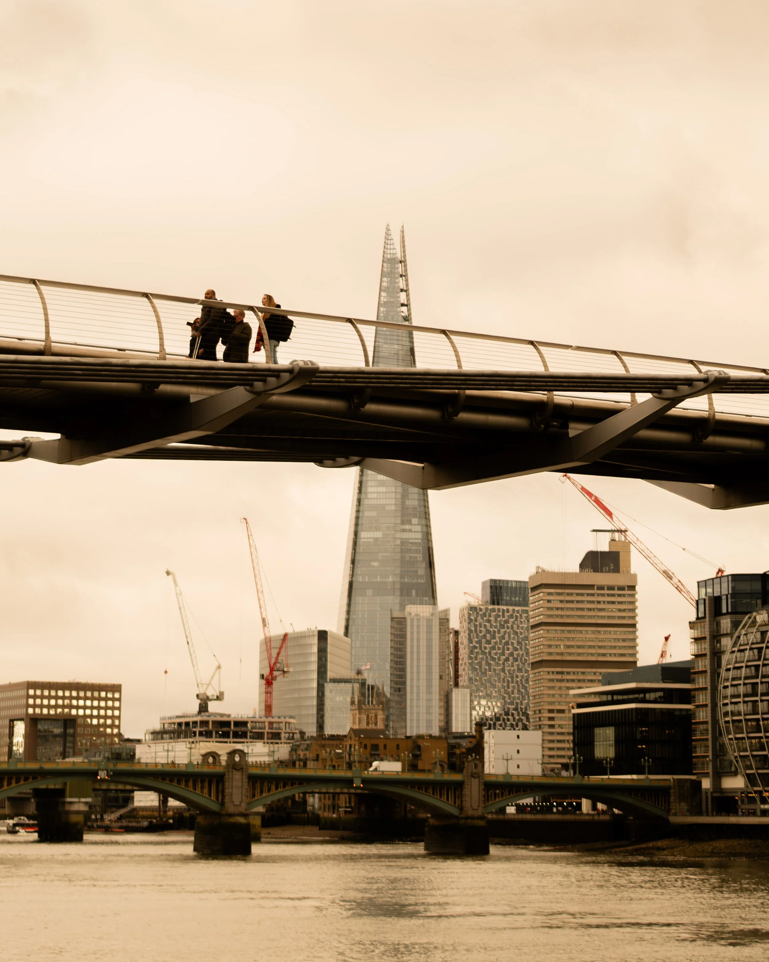 People walking on a modern pedestrian bridge over the River Thames with the London city skyline, including The Shard, in the background. Lionel Chu - Hotel & Travel Photographer