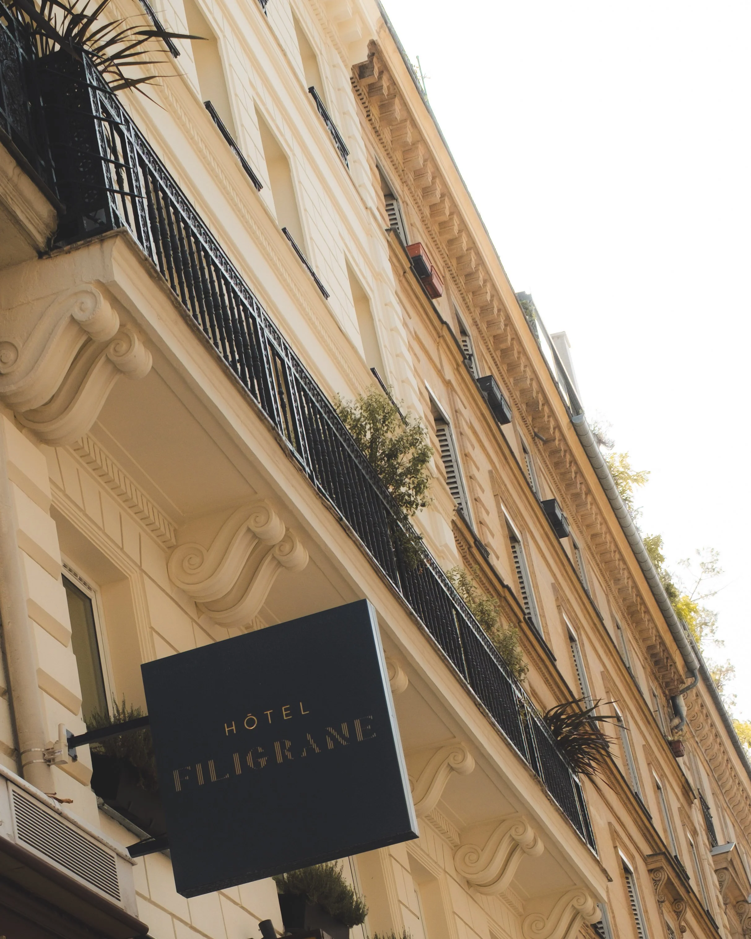 Street view of a European-style hotel building with ornate balconies, large windows, and classic architectural details. There is a hanging sign with the word 'hotel' partially visible.